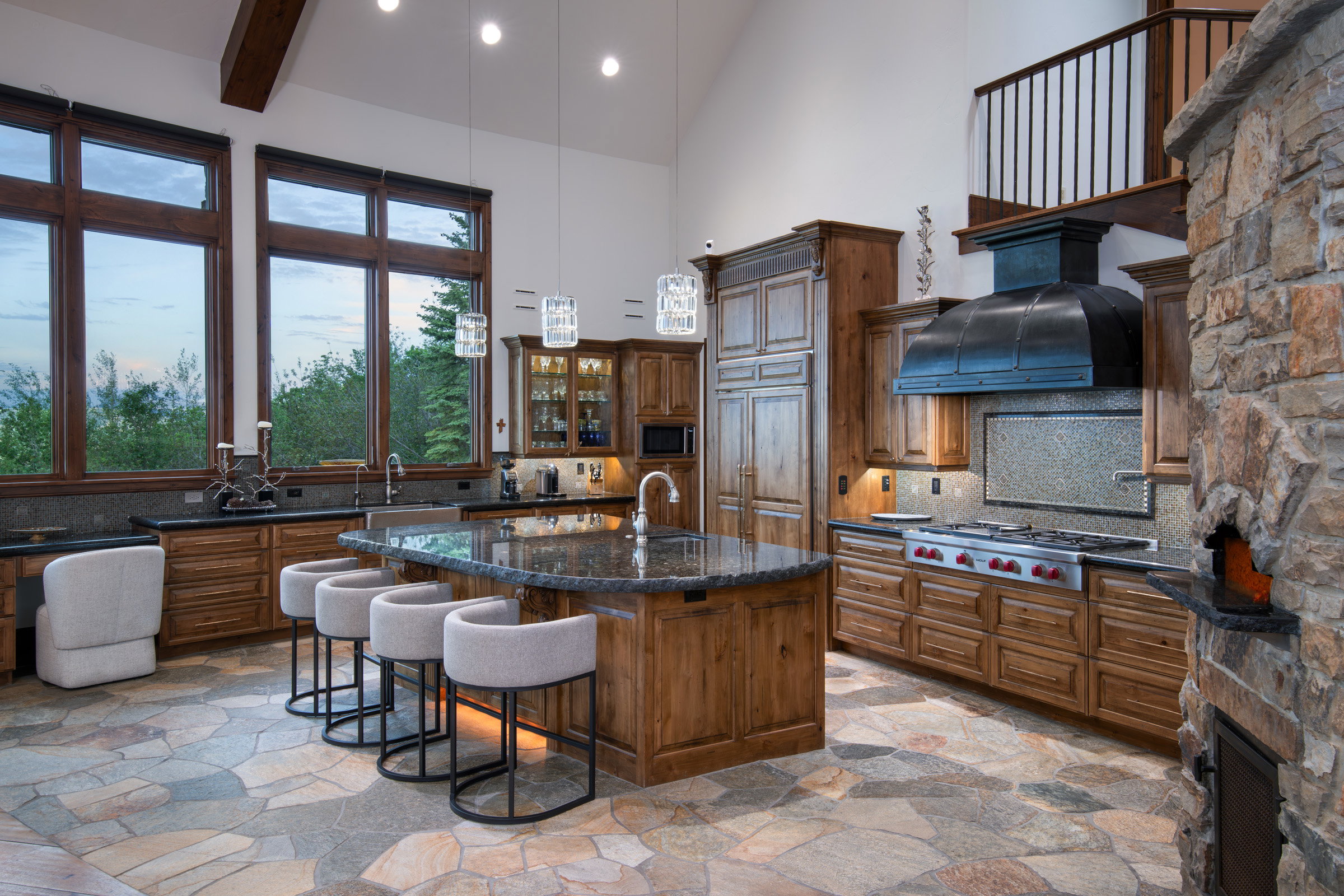 Spacious kitchen featuring a large central island with seating, natural wood cabinetry, dark stone countertops, and a professional-grade range with a custom hood