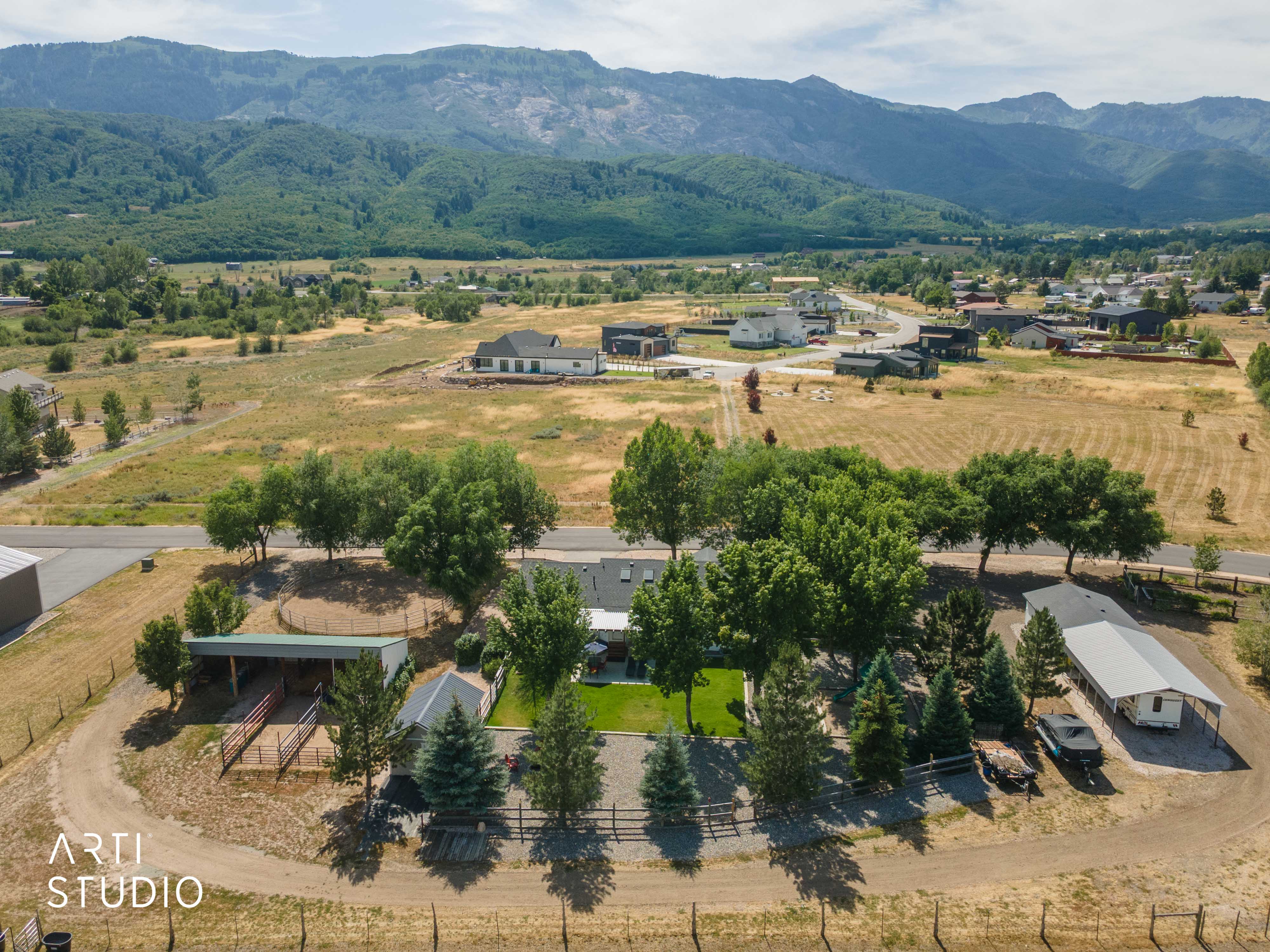 Expansive property featuring a central residence, multiple accessory structures, mature trees, and a dirt driveway