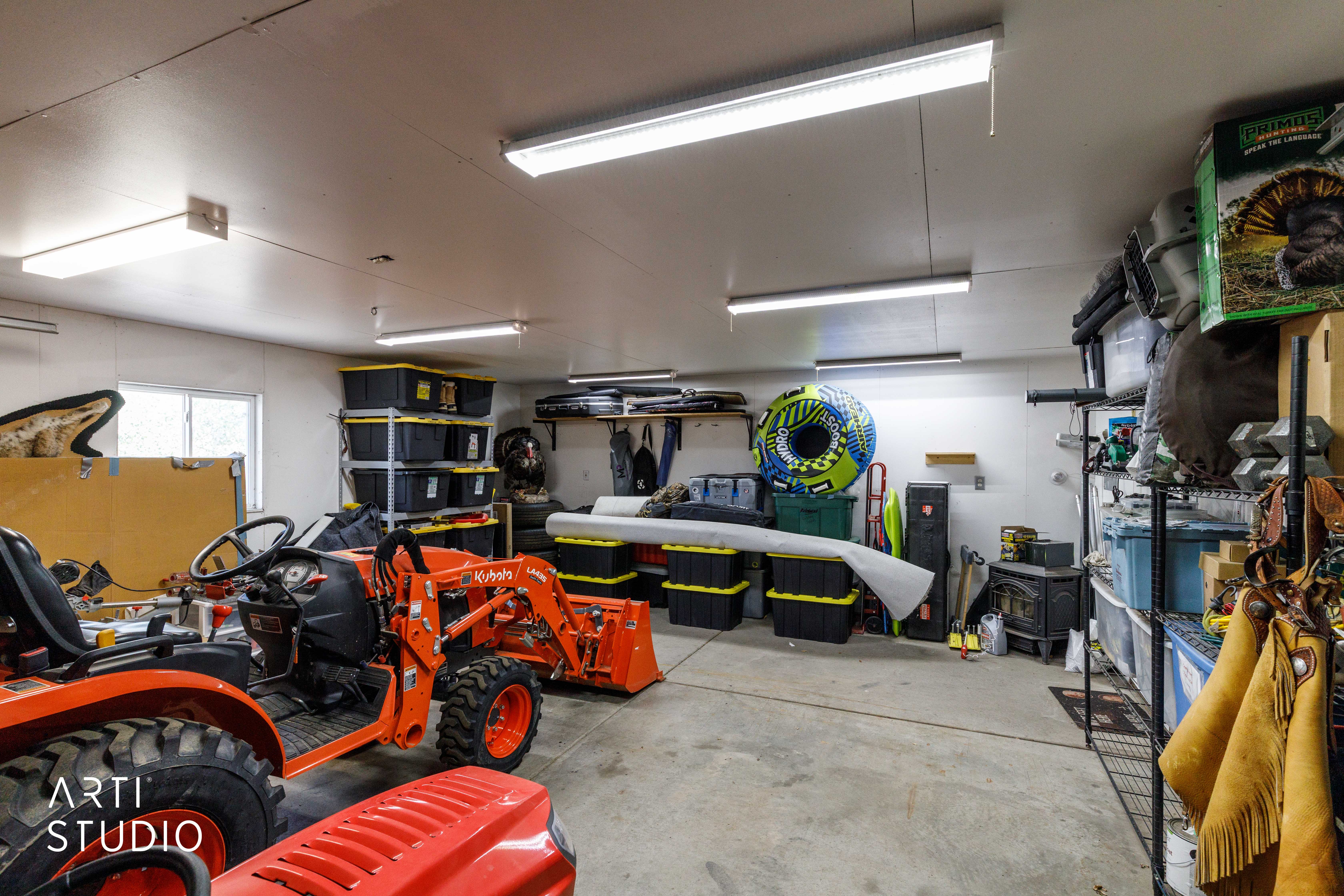 Spacious garage with multiple overhead fluorescent light fixtures, a concrete floor, white painted walls, and built-in shelving units