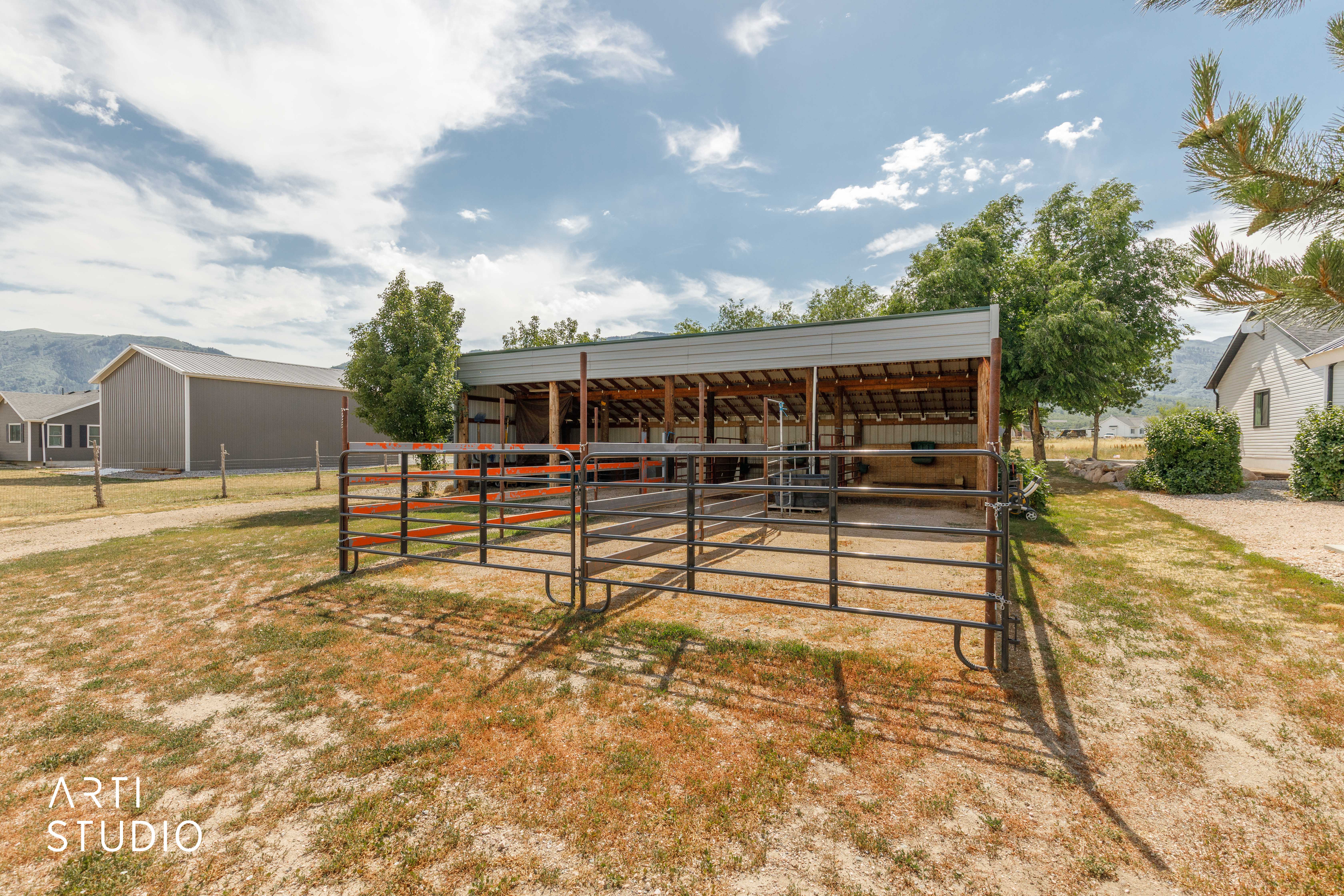 Covered livestock shelter with metal fencing, open-air design, and gravel flooring