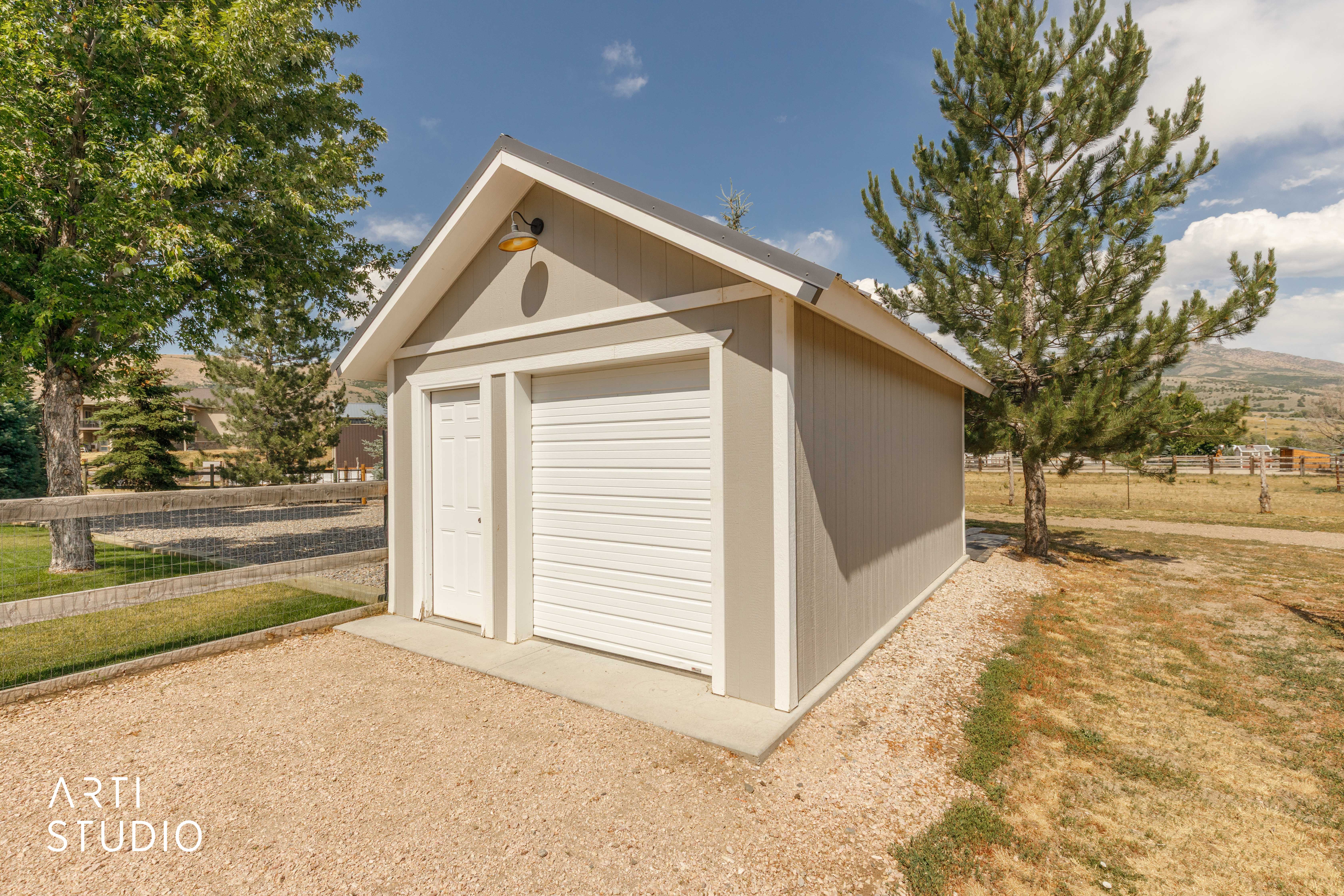 Freestanding outbuilding featuring light grey siding, white trim, a gabled roof, and a single garage door