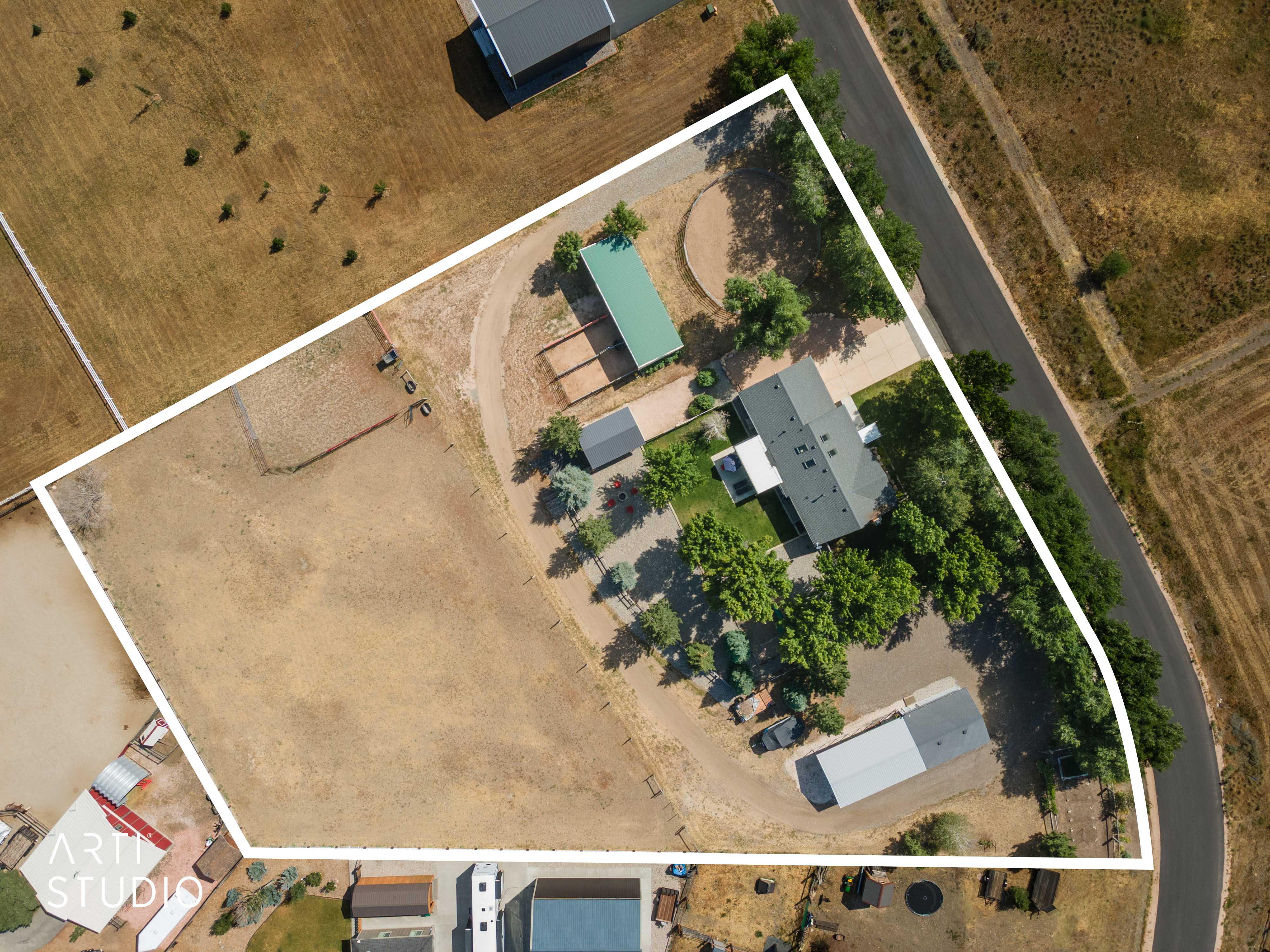 Aerial depiction of the property featuring a main residence with a dark gray roof, multiple outbuildings, mature trees, and expansive land