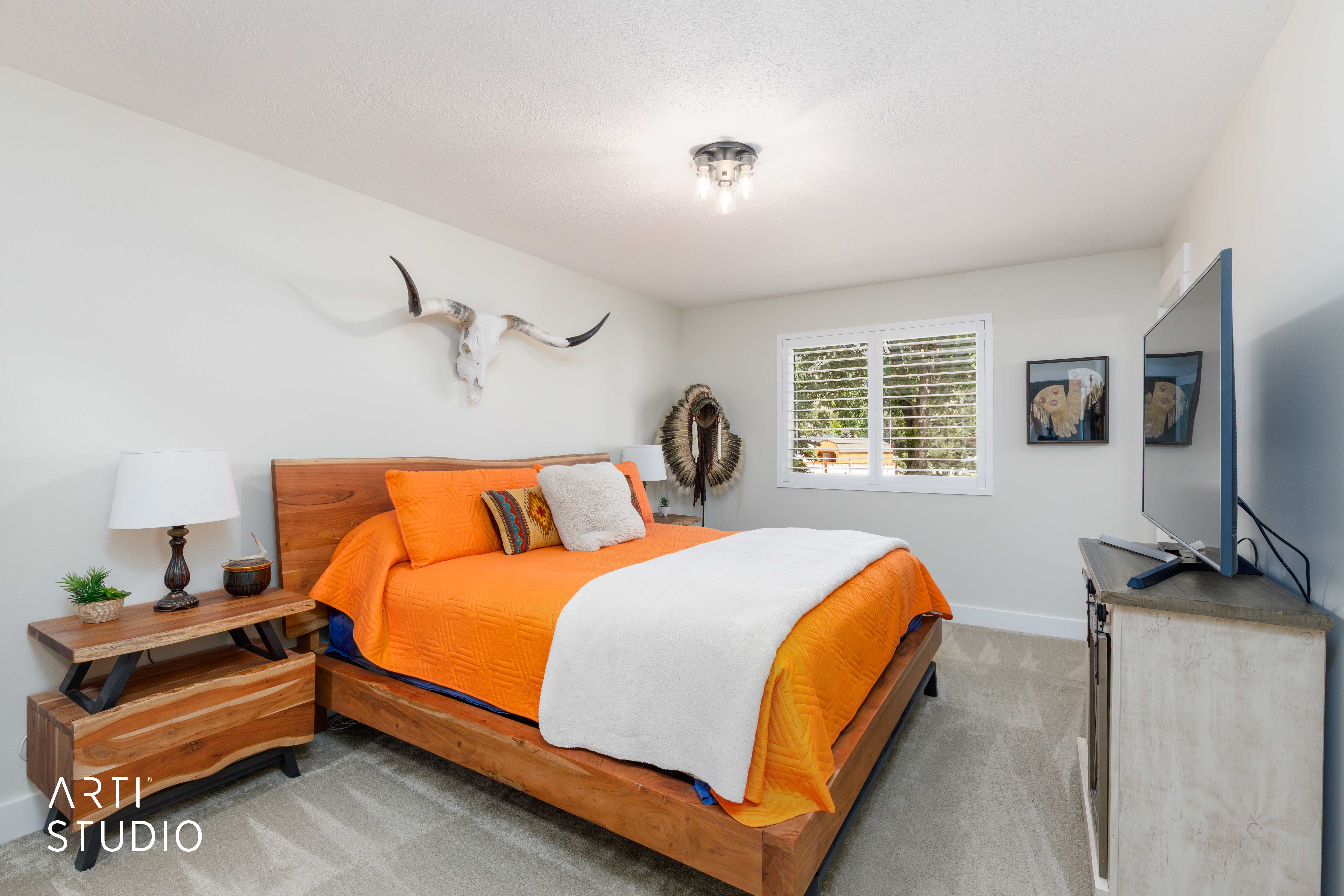 Bedroom featuring light-colored walls, carpeted flooring, and a white-framed window with plantation shutters
