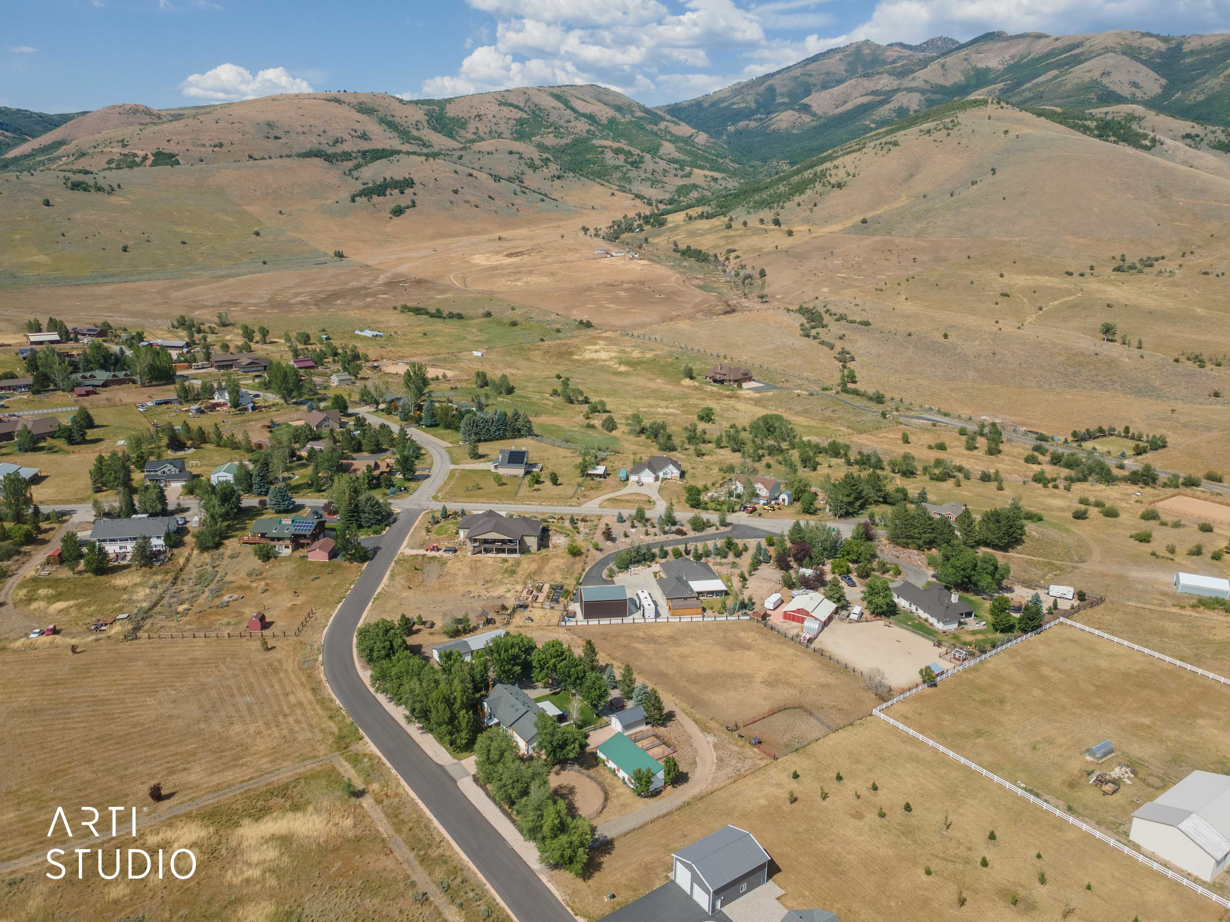 Expansive mountain landscape featuring a community of homes, paved roads, open fields, and various outbuildings