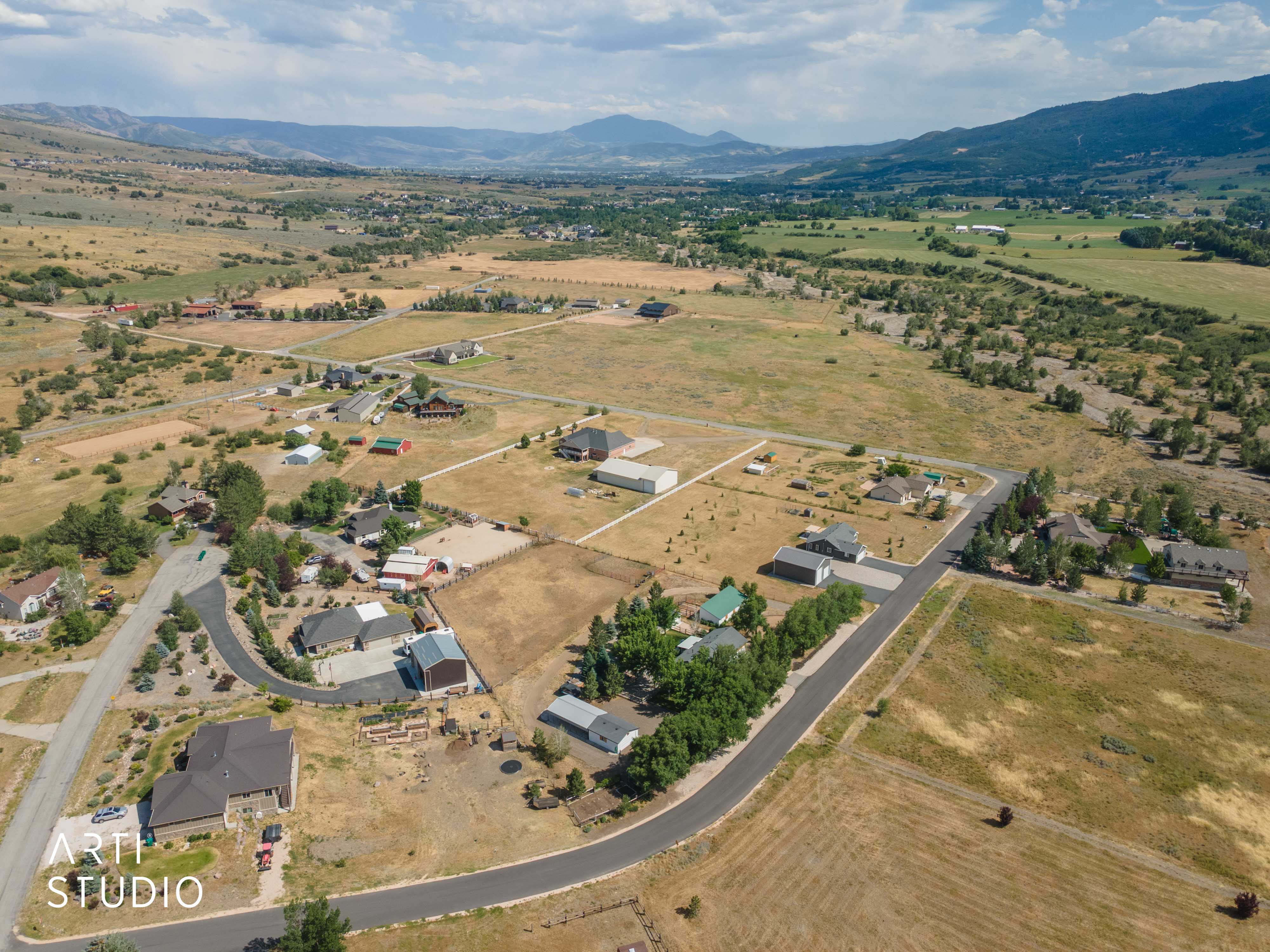 Expansive rural landscape featuring scattered residential properties, mature trees, open fields, and distant mountains