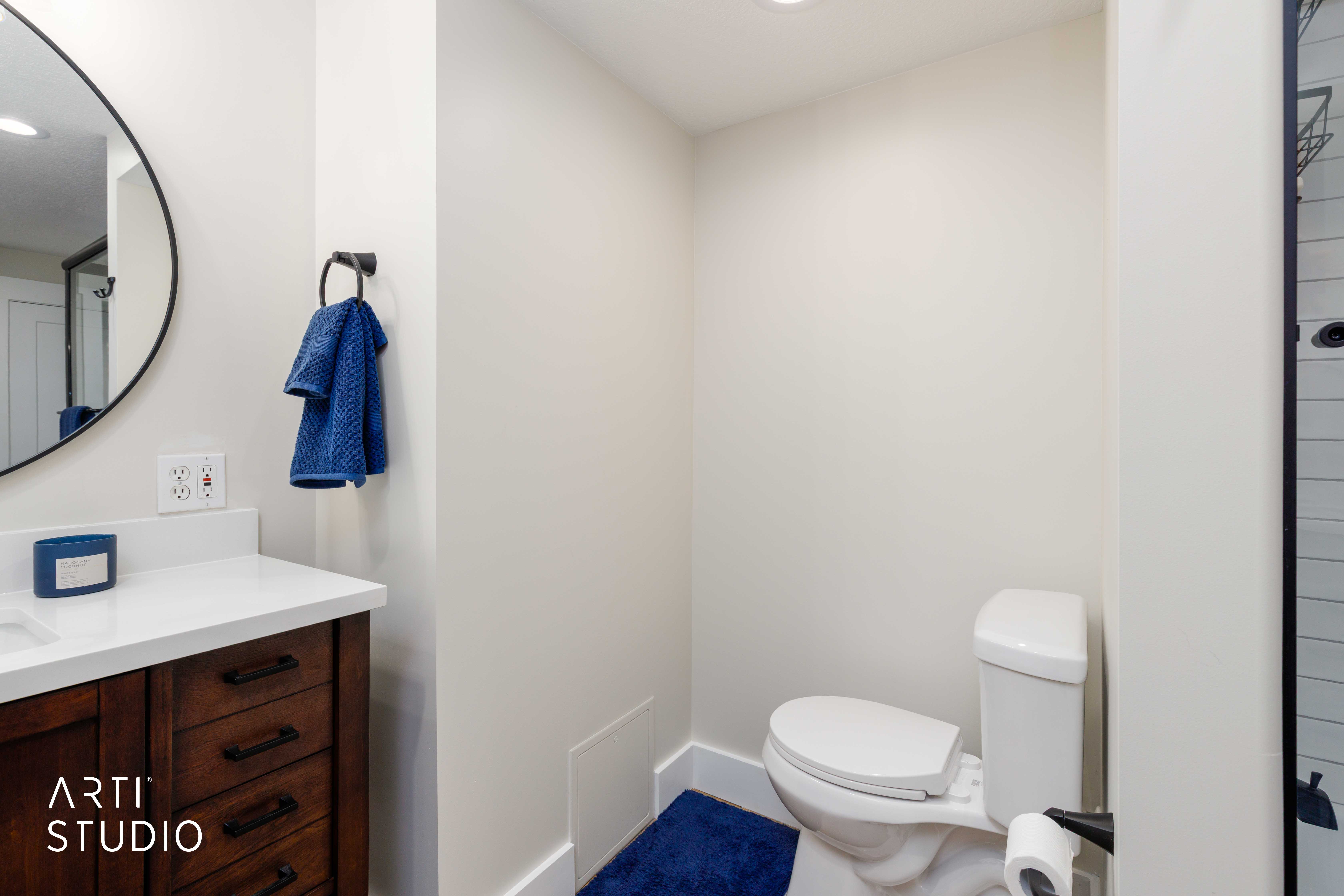 Bathroom featuring a wood-finish vanity with white countertop, round black-framed mirror, recessed lighting, and a white toilet