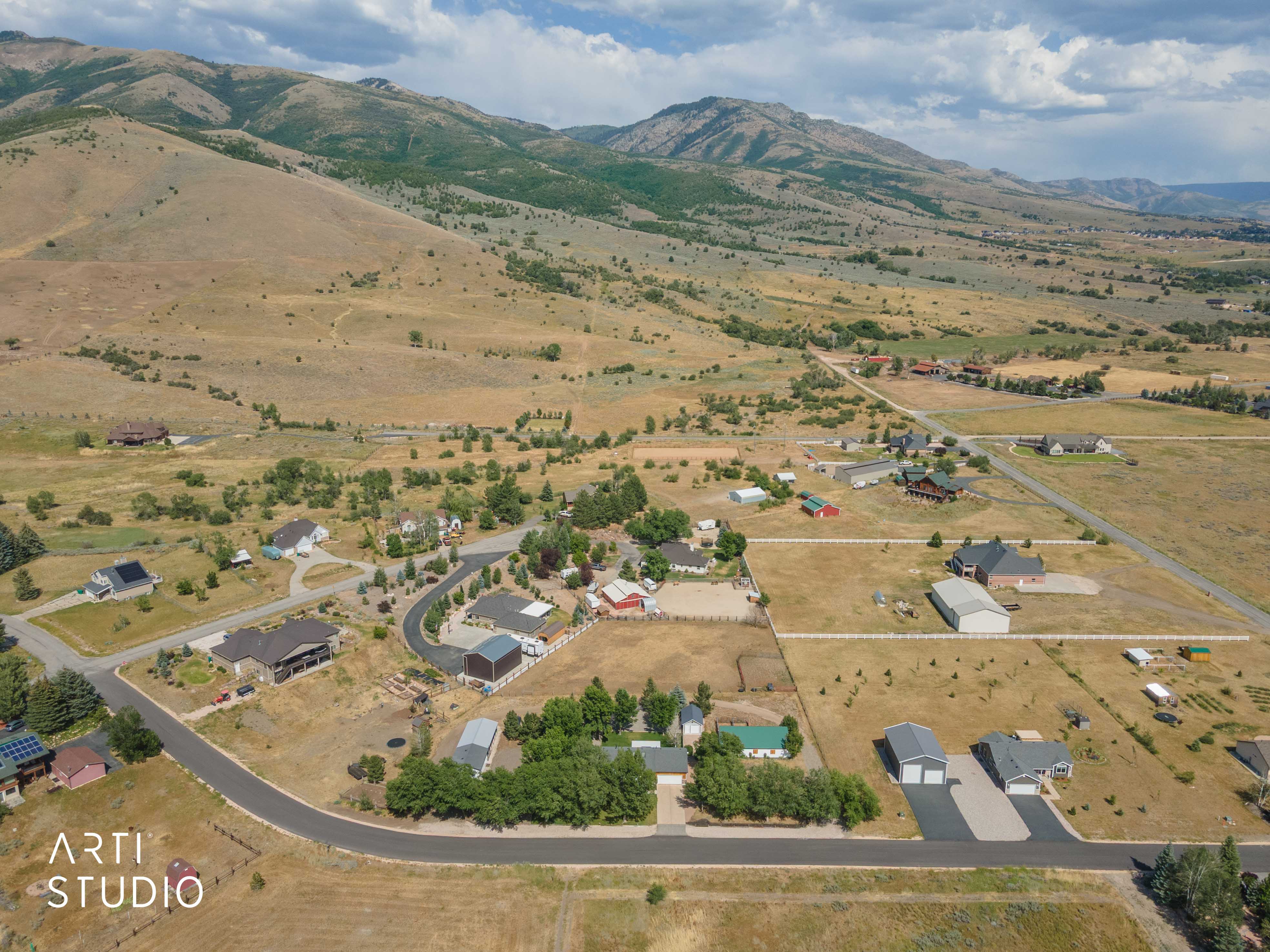 Expansive rural landscape featuring a mountainous backdrop, established residential properties, paved roads, and open land parcels