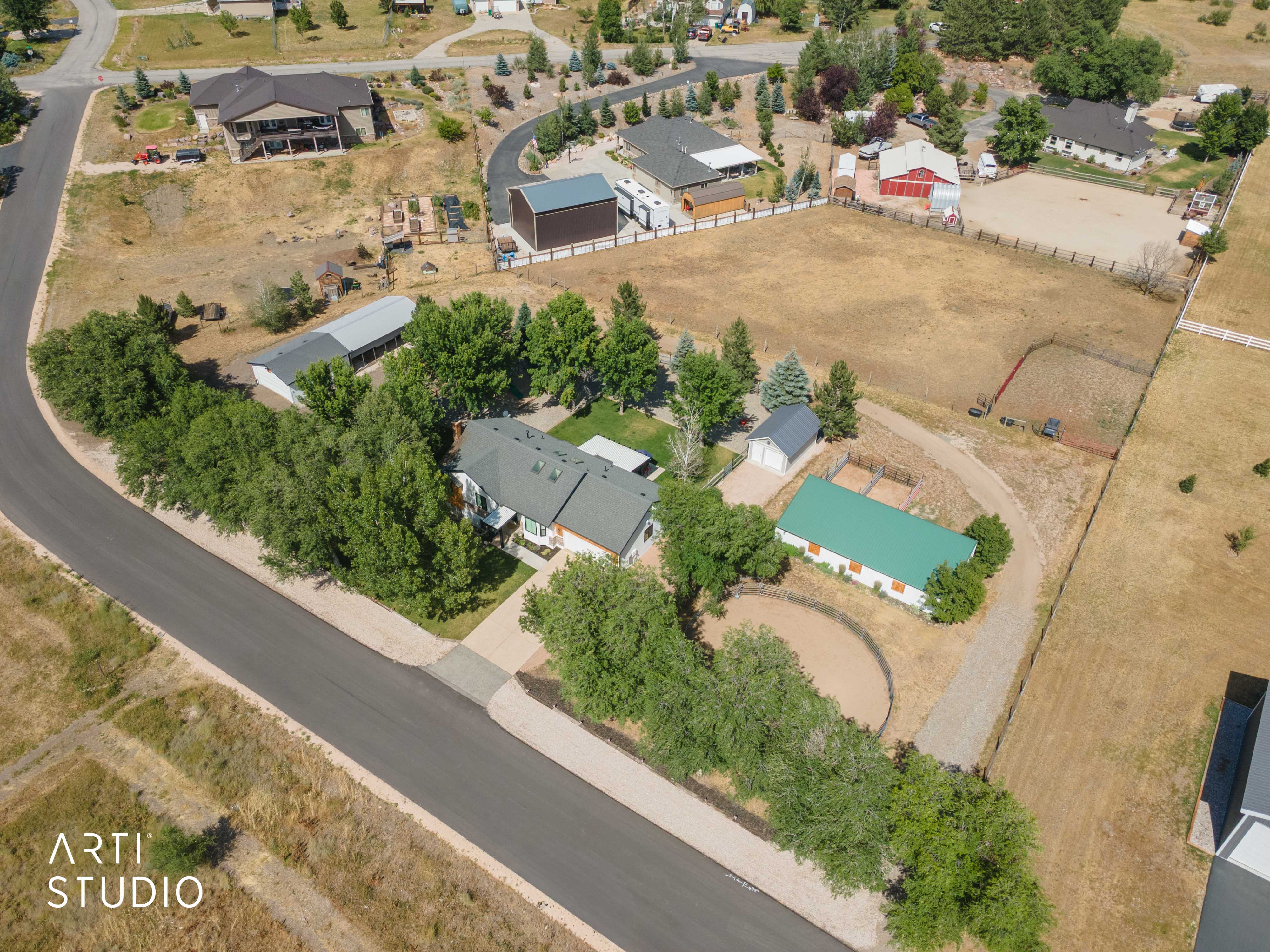 Expansive property featuring a main residence with a dark-pitched roof, a large green-roofed outbuilding, a white detached garage, and a circular fenced area