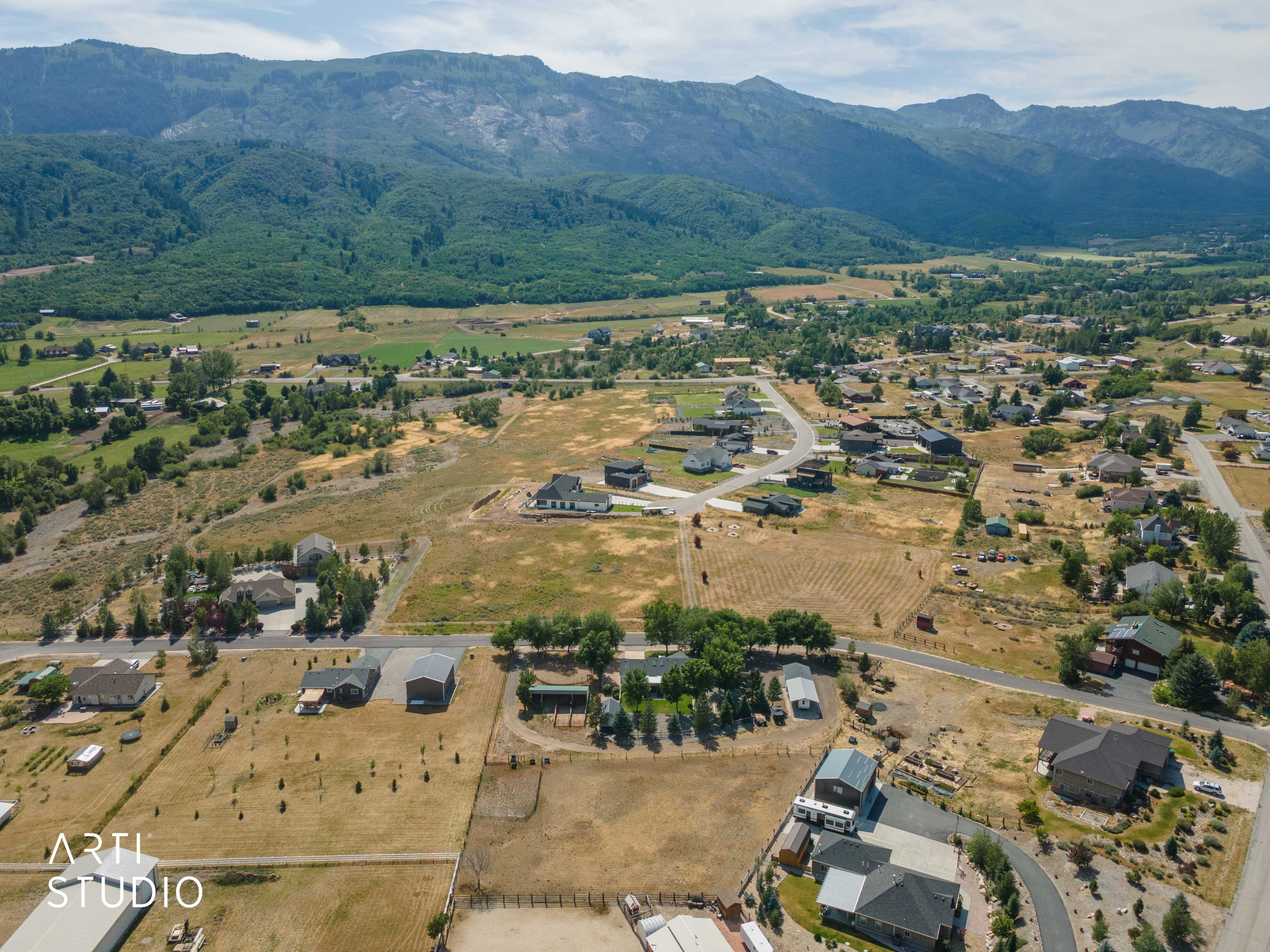 Expansive rural landscape featuring a mix of residential properties, undeveloped land, and mature trees, all set against a backdrop of prominent mountains