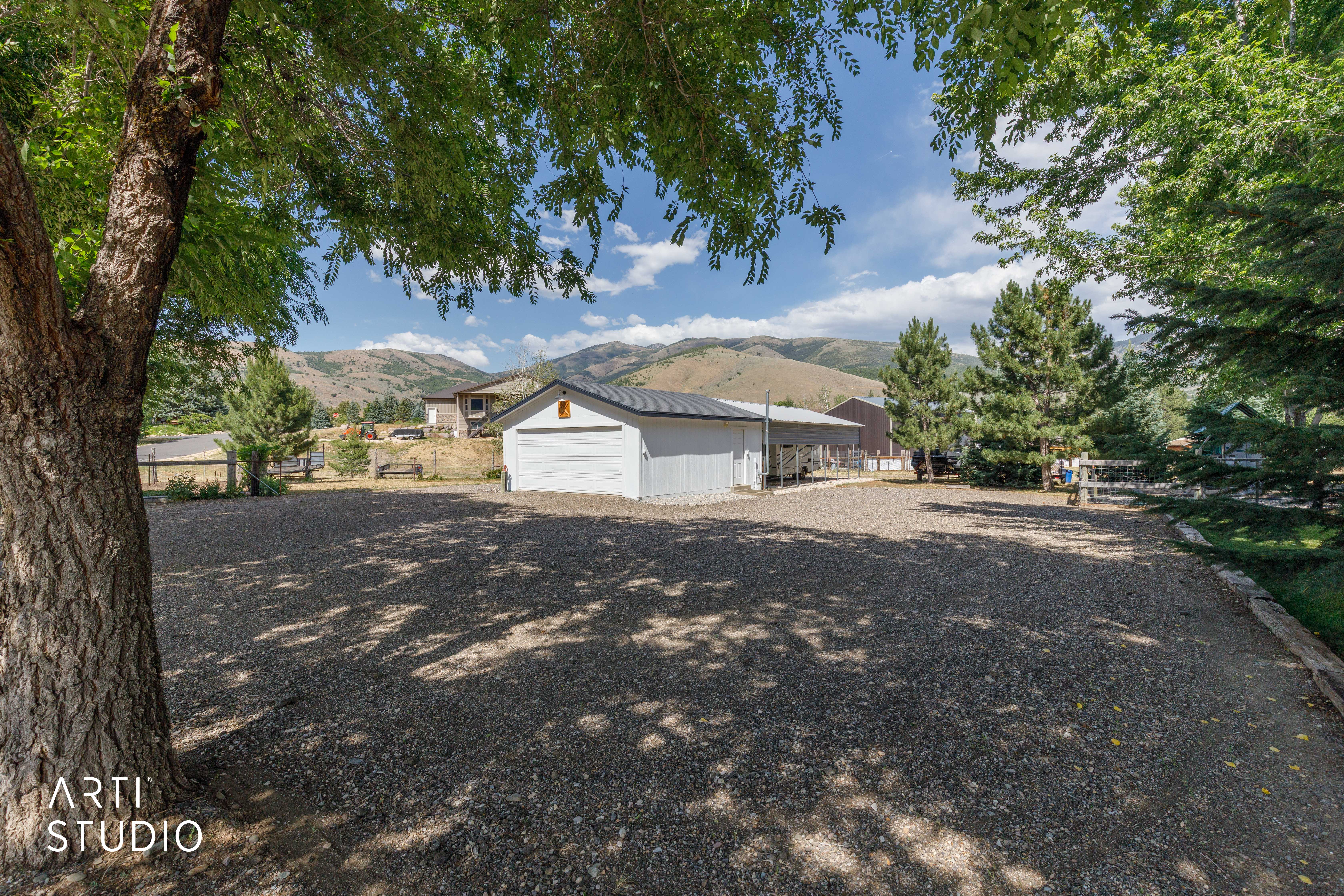 Gravel parking area featuring mature trees, a detached garage, and distant mountain scenery