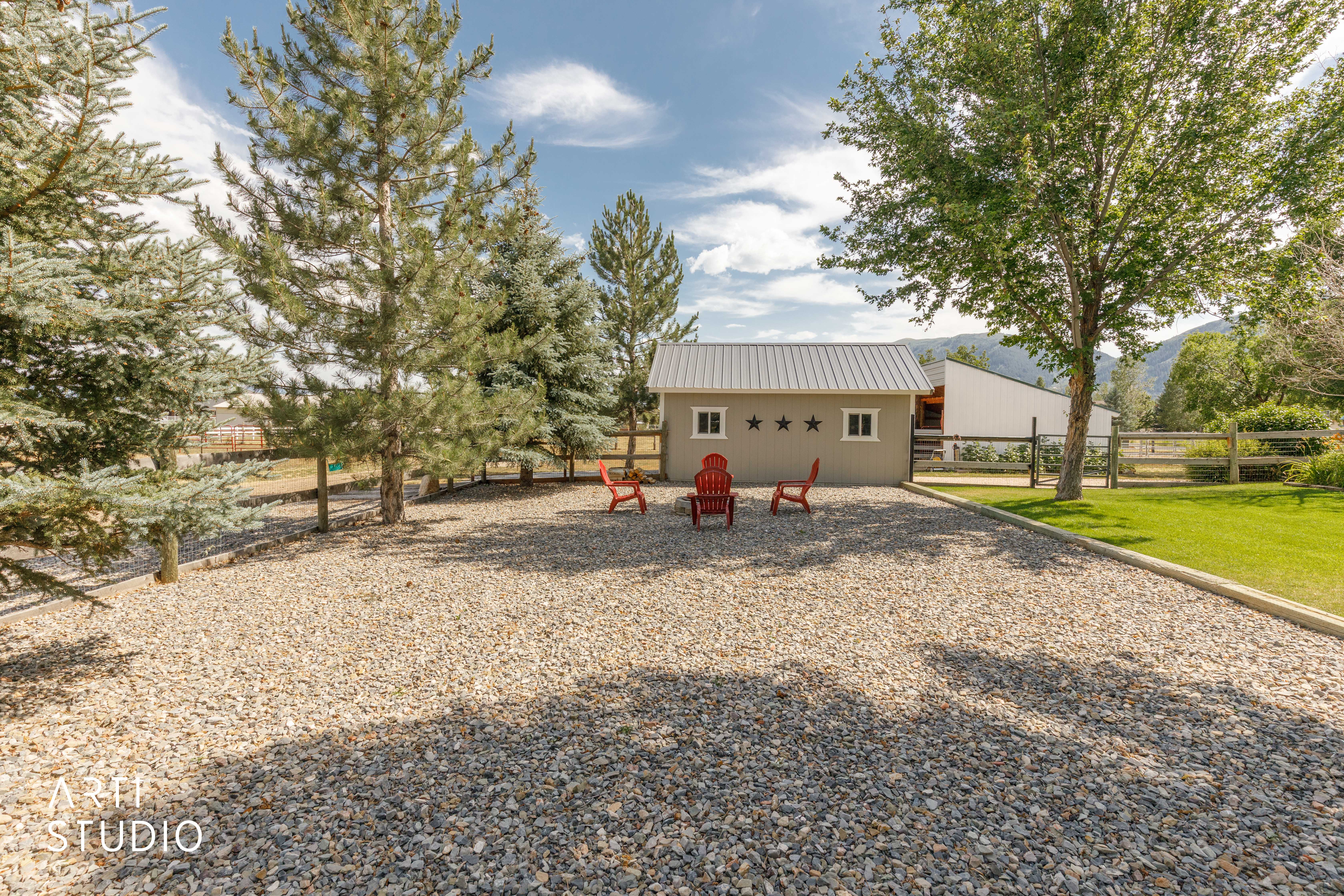 Gravel outdoor space featuring a detached auxiliary building with a metal roof, multiple windows, and decorative star accents
