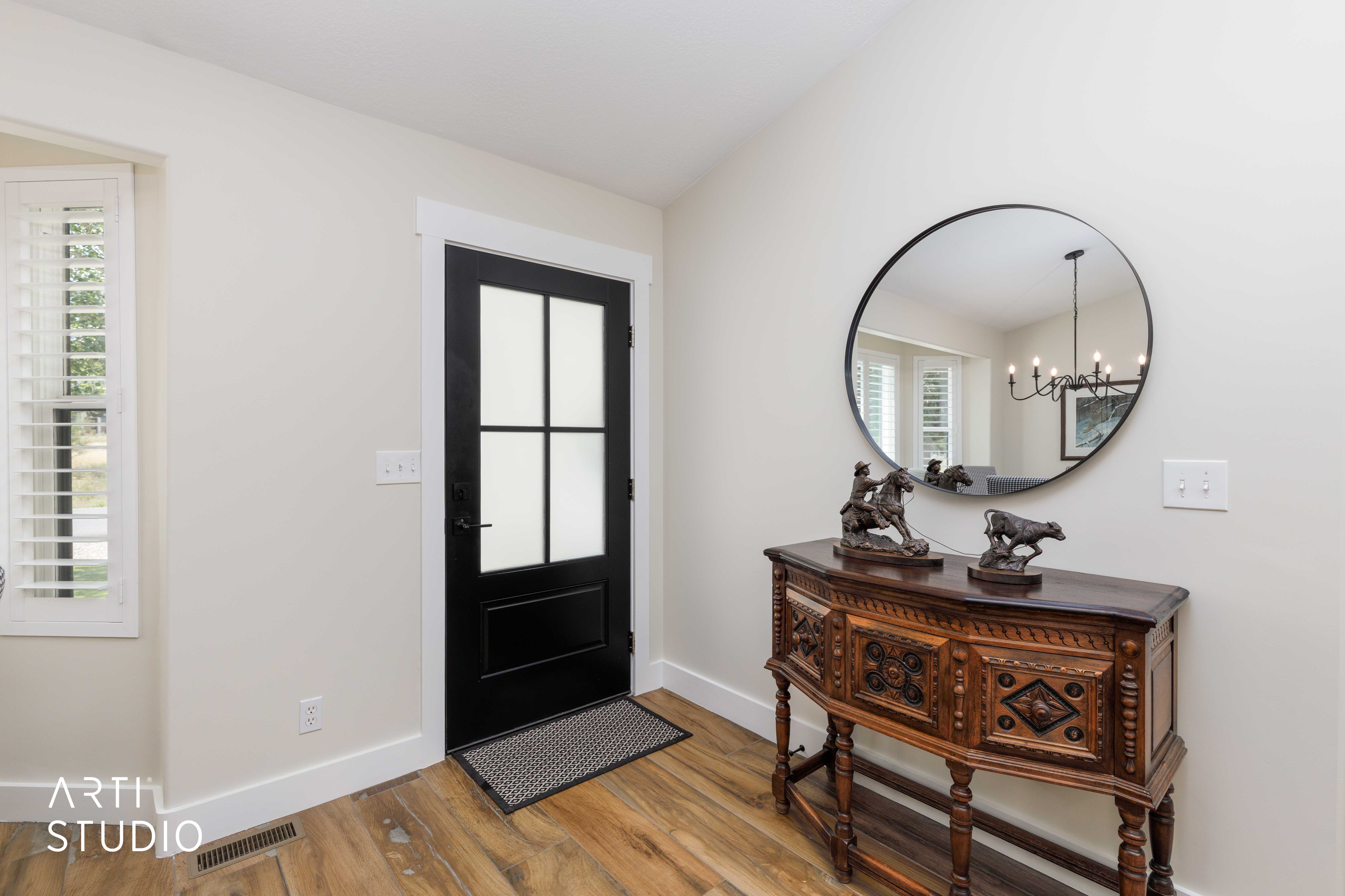 Entryway featuring a black paneled door with frosted glass, wood-finish flooring, and white plantation shutters on the window