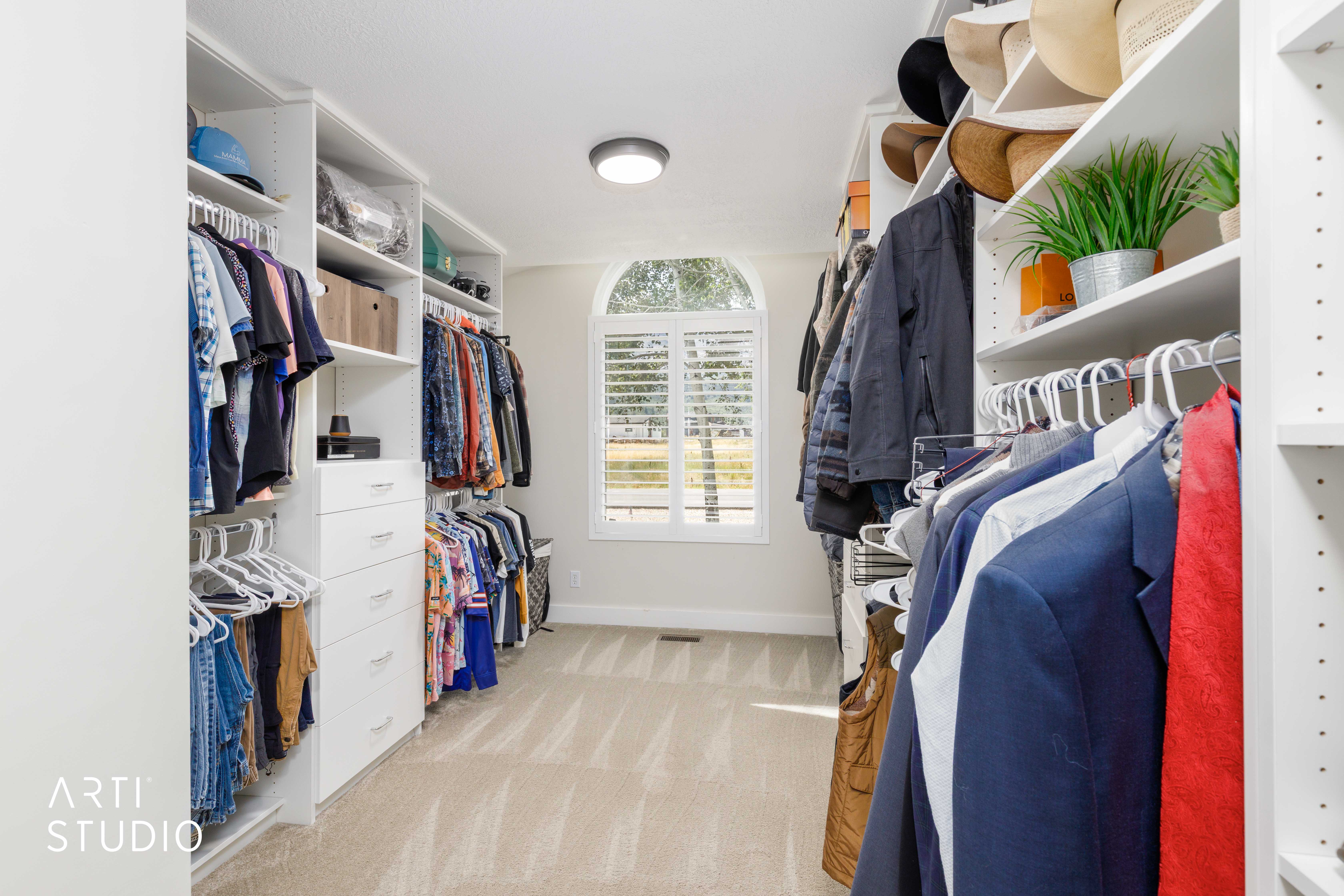 Walk-in closet featuring extensive built-in shelving, multiple hanging rods, integrated drawer storage, arched window with plantation shutters, and recessed ceiling lighting