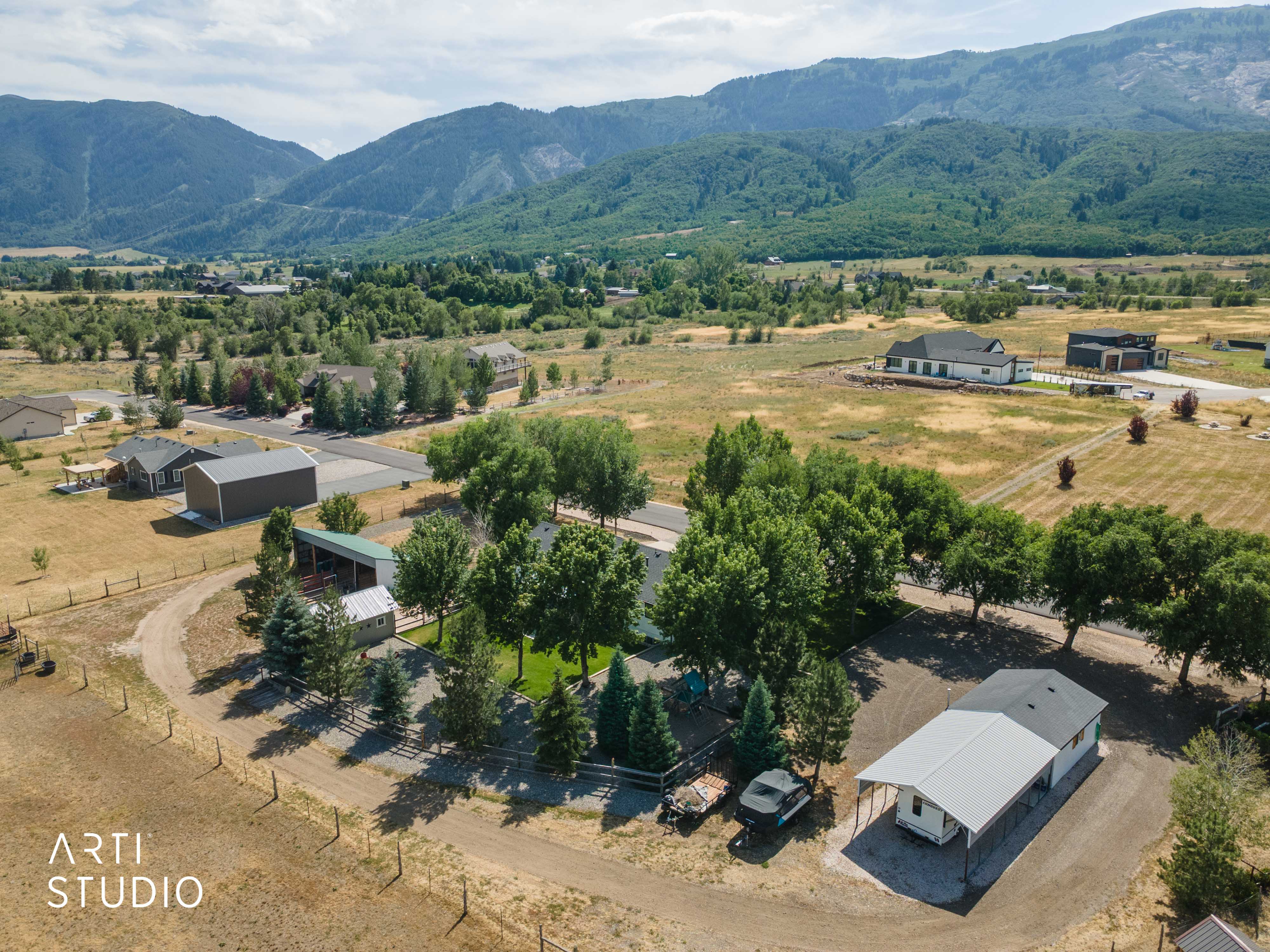 Expansive property featuring a gravel driveway, mature trees, and a detached building with an attached carport