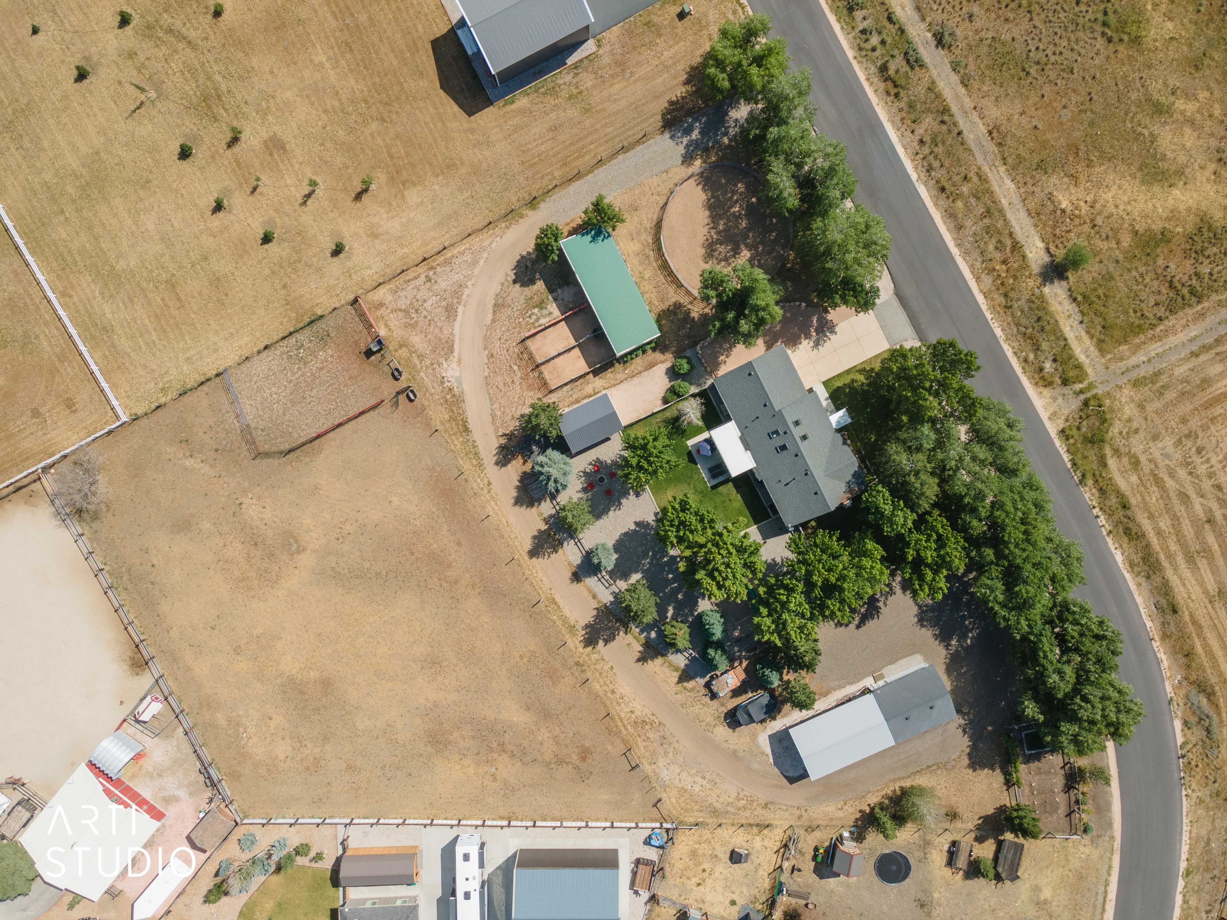 Expansive property featuring a main residence with a dark-pitched roof, paved driveway, mature perimeter trees, and multiple outbuildings