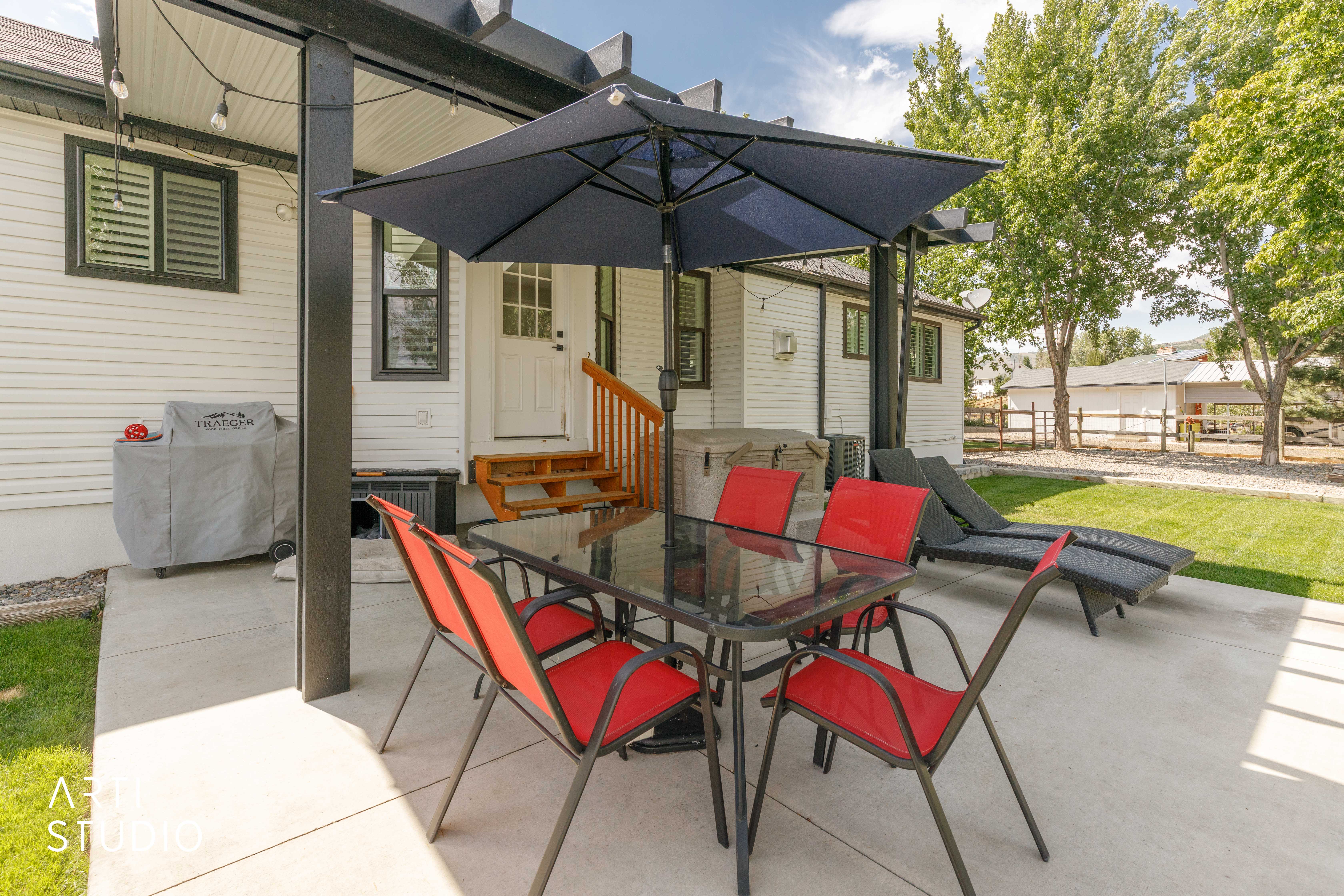 Poured concrete patio featuring a black pergola, white siding, and a manicured lawn