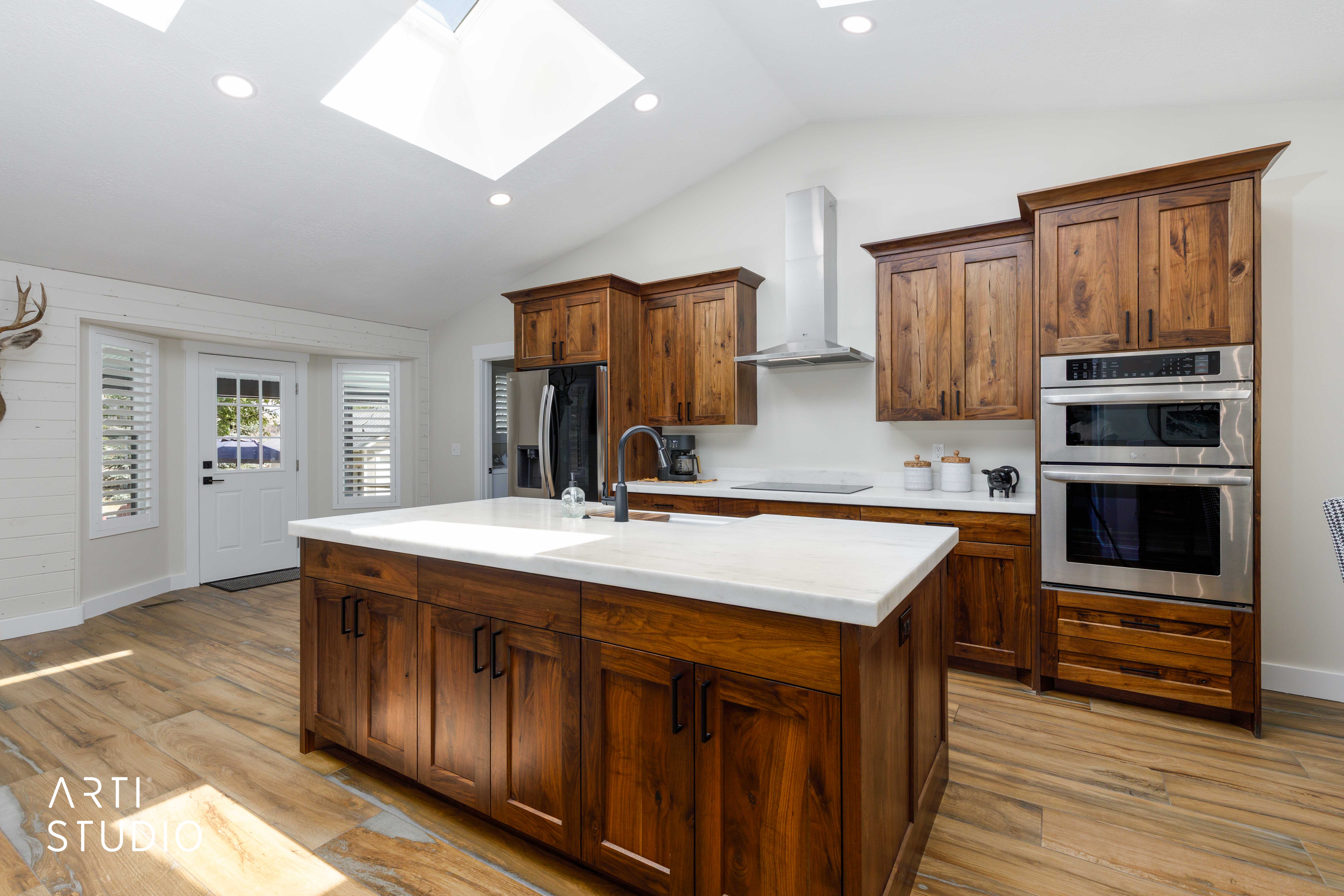 Spacious kitchen featuring an expansive center island with a light-toned countertop, wood-finish flooring, recessed lighting, and dual skylights