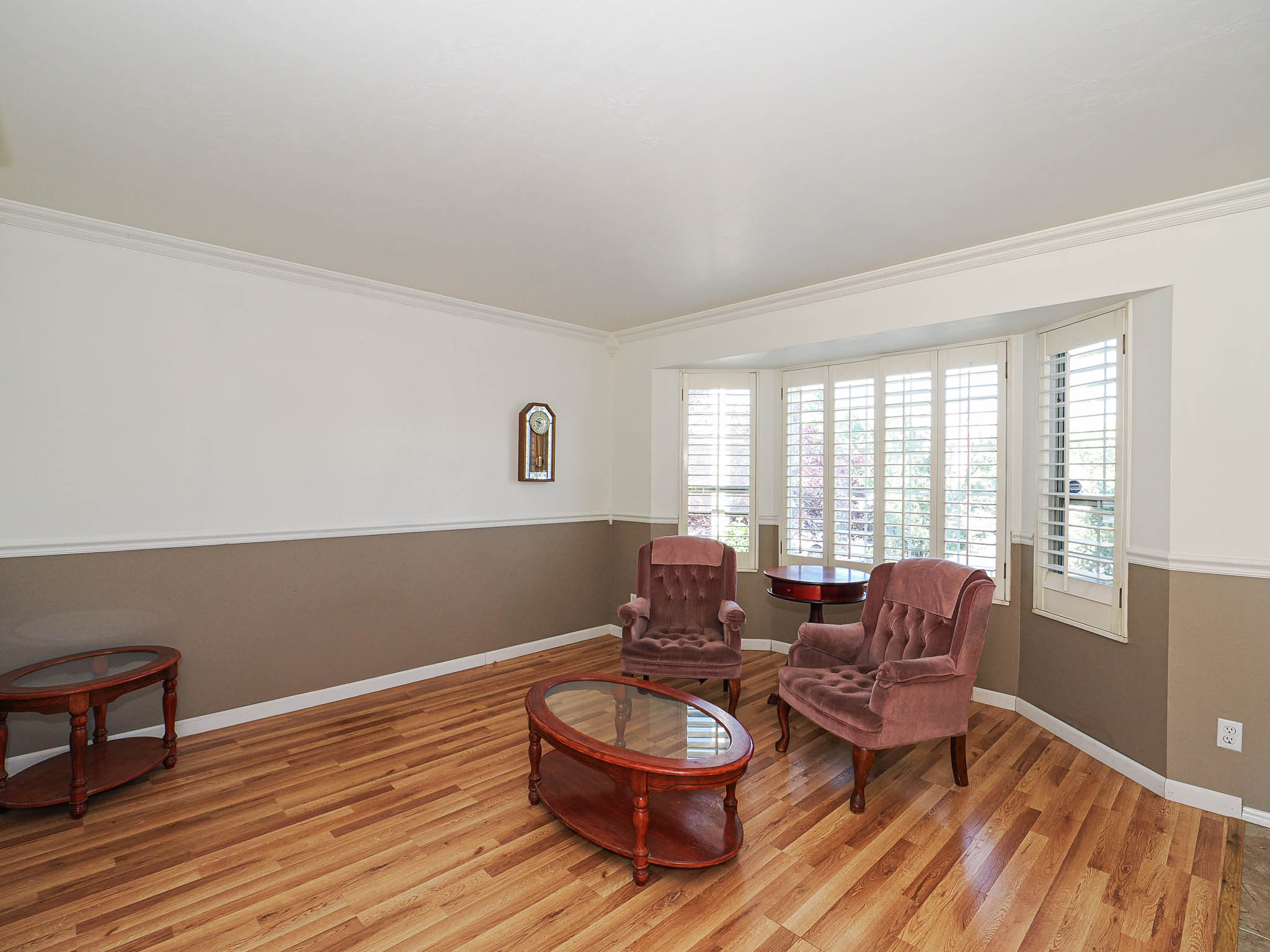 Spacious interior featuring wood-finish flooring, two-tone wall paint, and a bay window with plantation shutters
