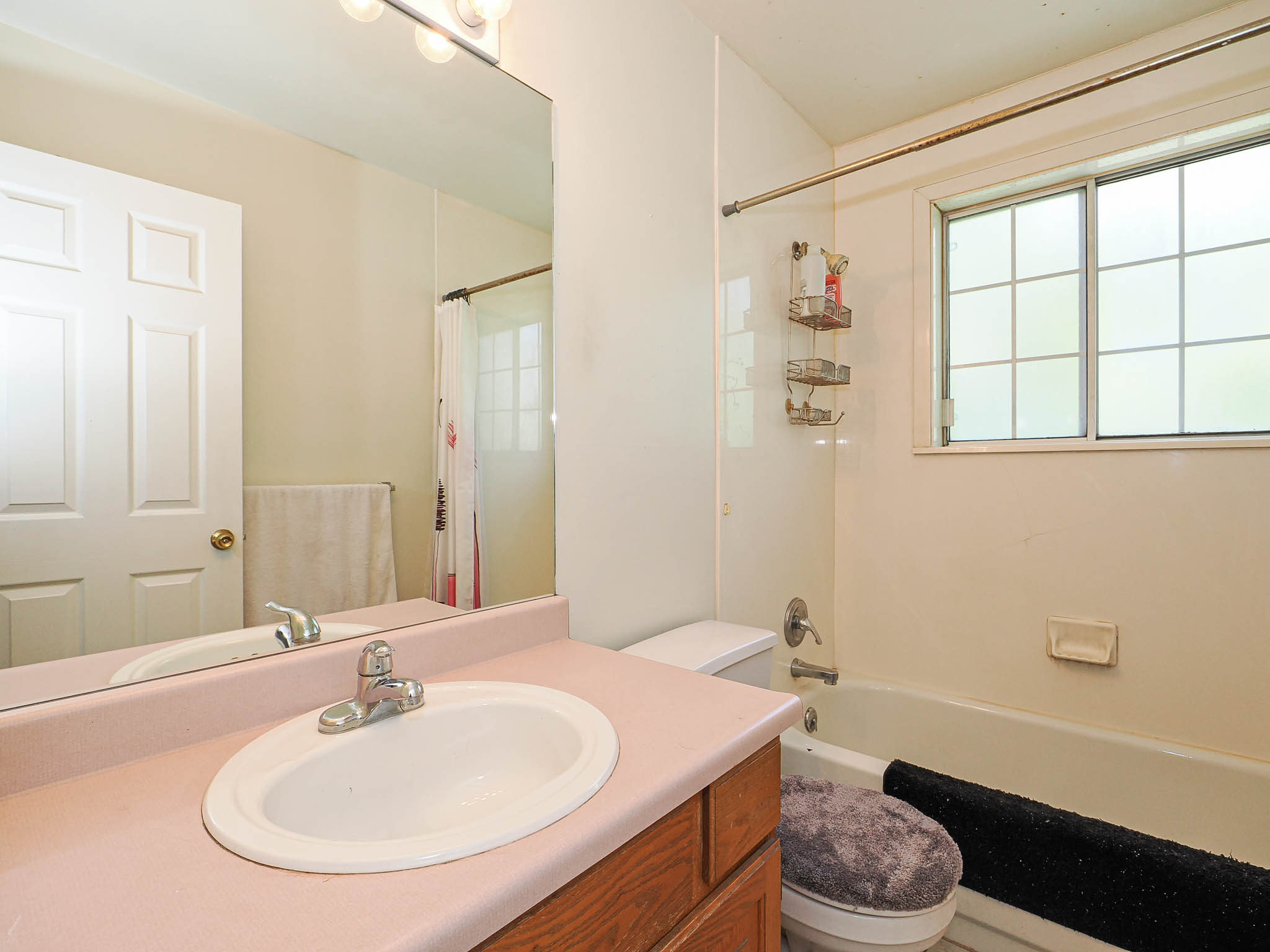 Full bathroom featuring a single vanity with an integrated sink, a large wall-mounted mirror, overhead vanity lighting, and a combination shower/bathtub with a window