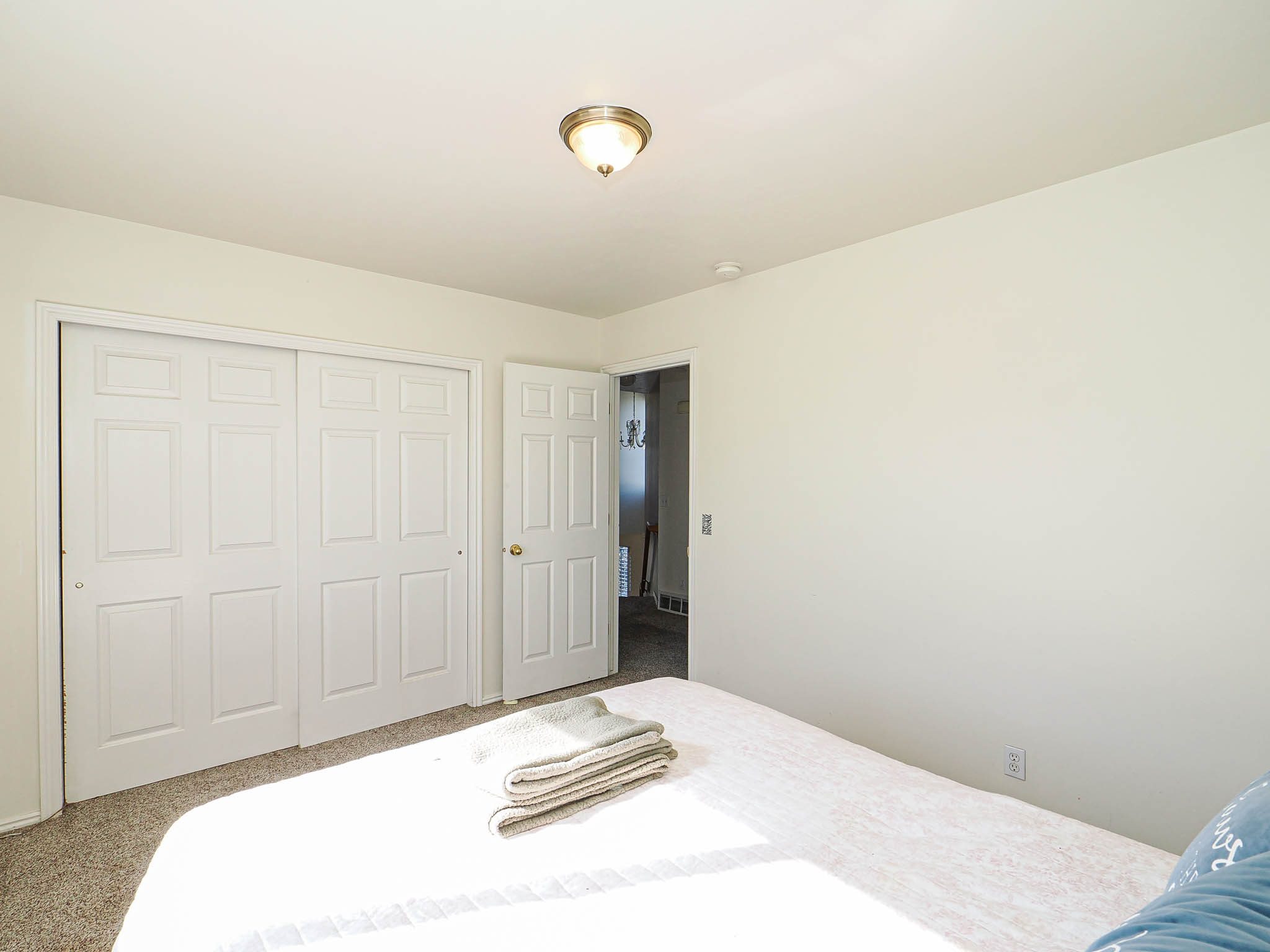 Bedroom featuring light neutral wall paint, carpet flooring, a flush-mount ceiling light fixture, and white bi-fold closet doors