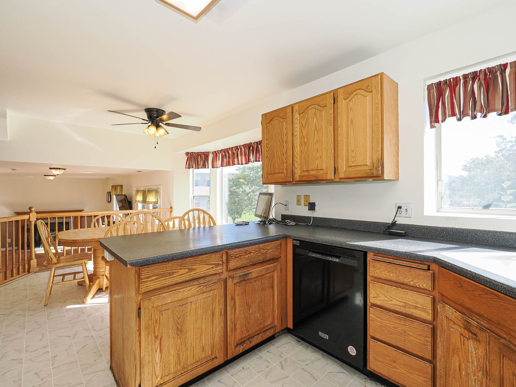 Kitchen featuring natural wood cabinetry, a built-in dishwasher, black countertops, and tile flooring