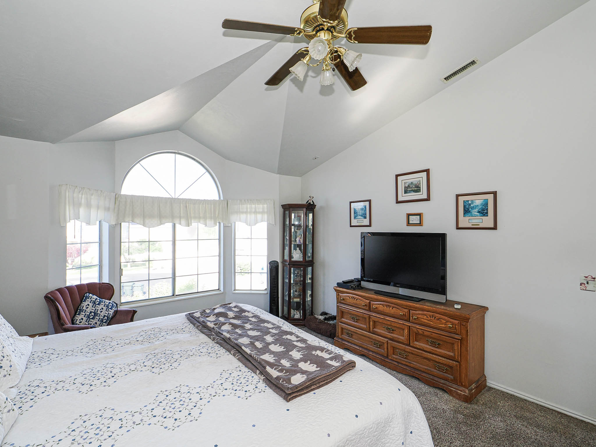 Vaulted ceiling with a ceiling fan, a large bay window, and an arched window feature