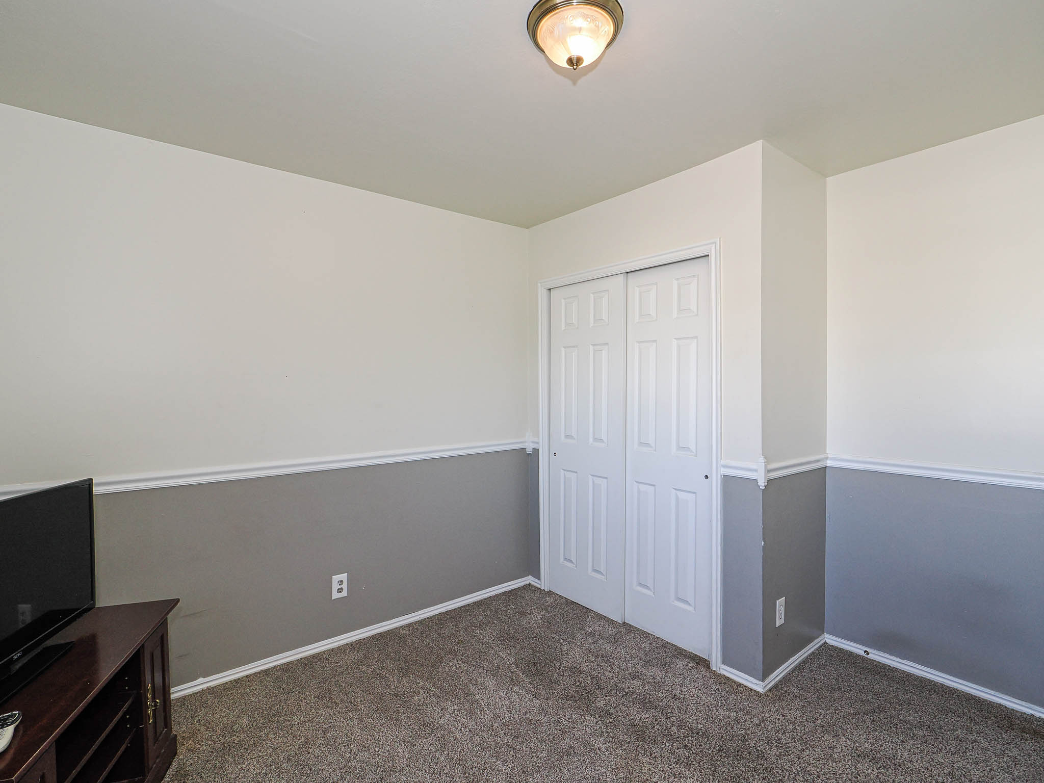 Room featuring white walls above a gray wainscoting, white baseboards, and neutral carpet