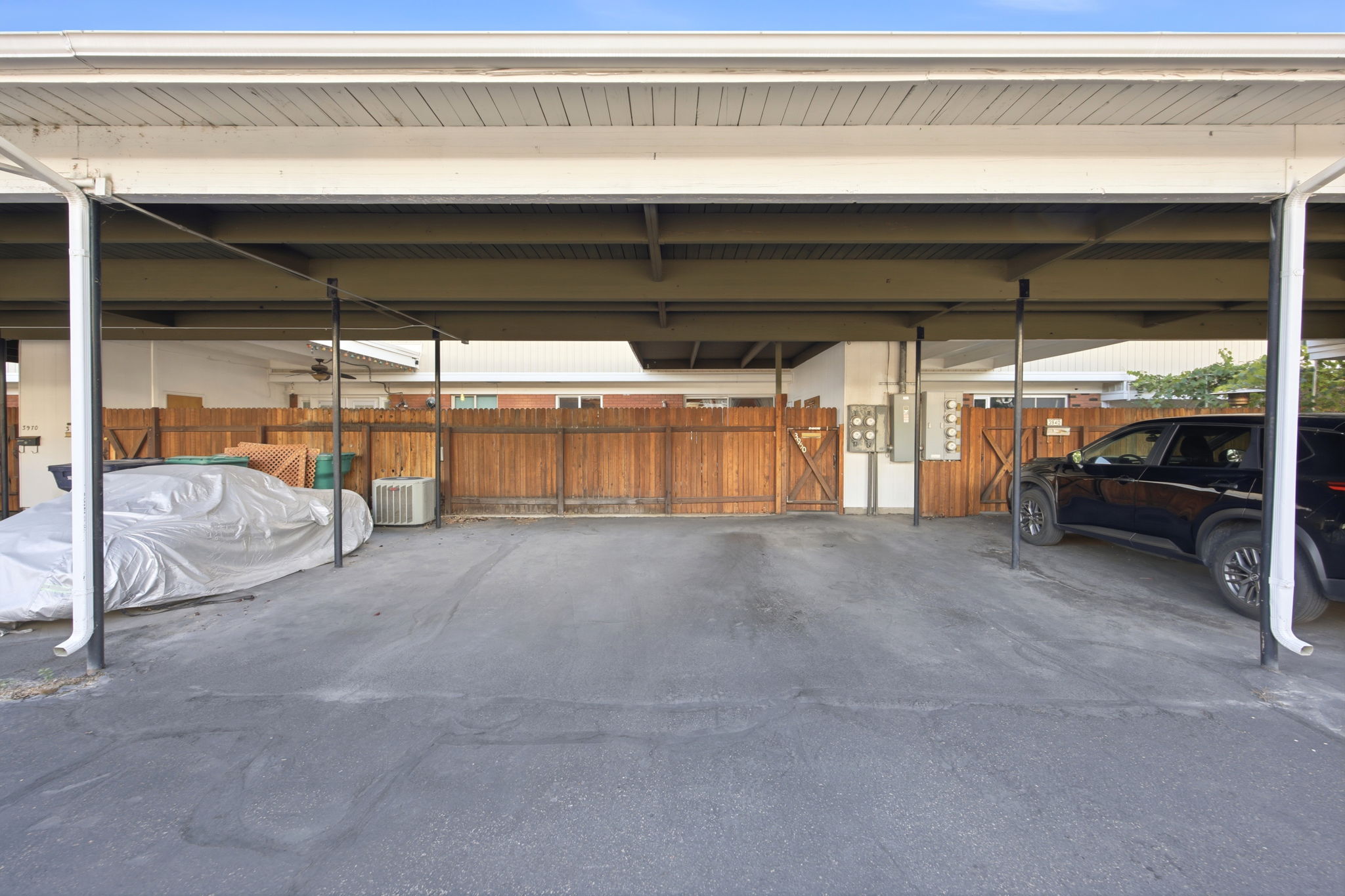Covered parking structure featuring multiple bays, a composite shingle roof, painted white fascia, and a wood fence perimeter