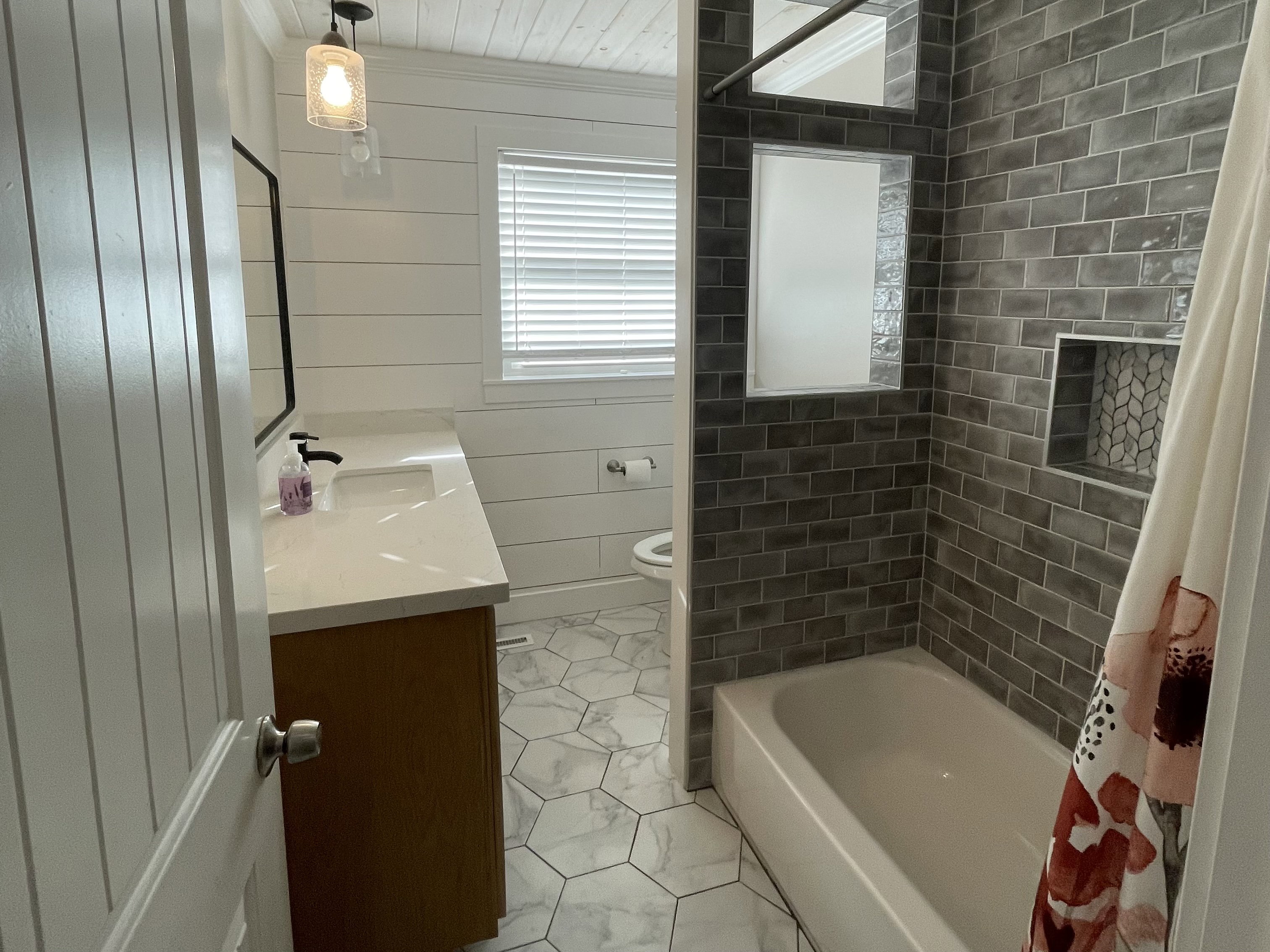 Bathroom featuring a vanity with an integrated sink and matte black faucet, shiplap walls, a tub/shower combination with subway tile surround, and hexagonal floor tiling