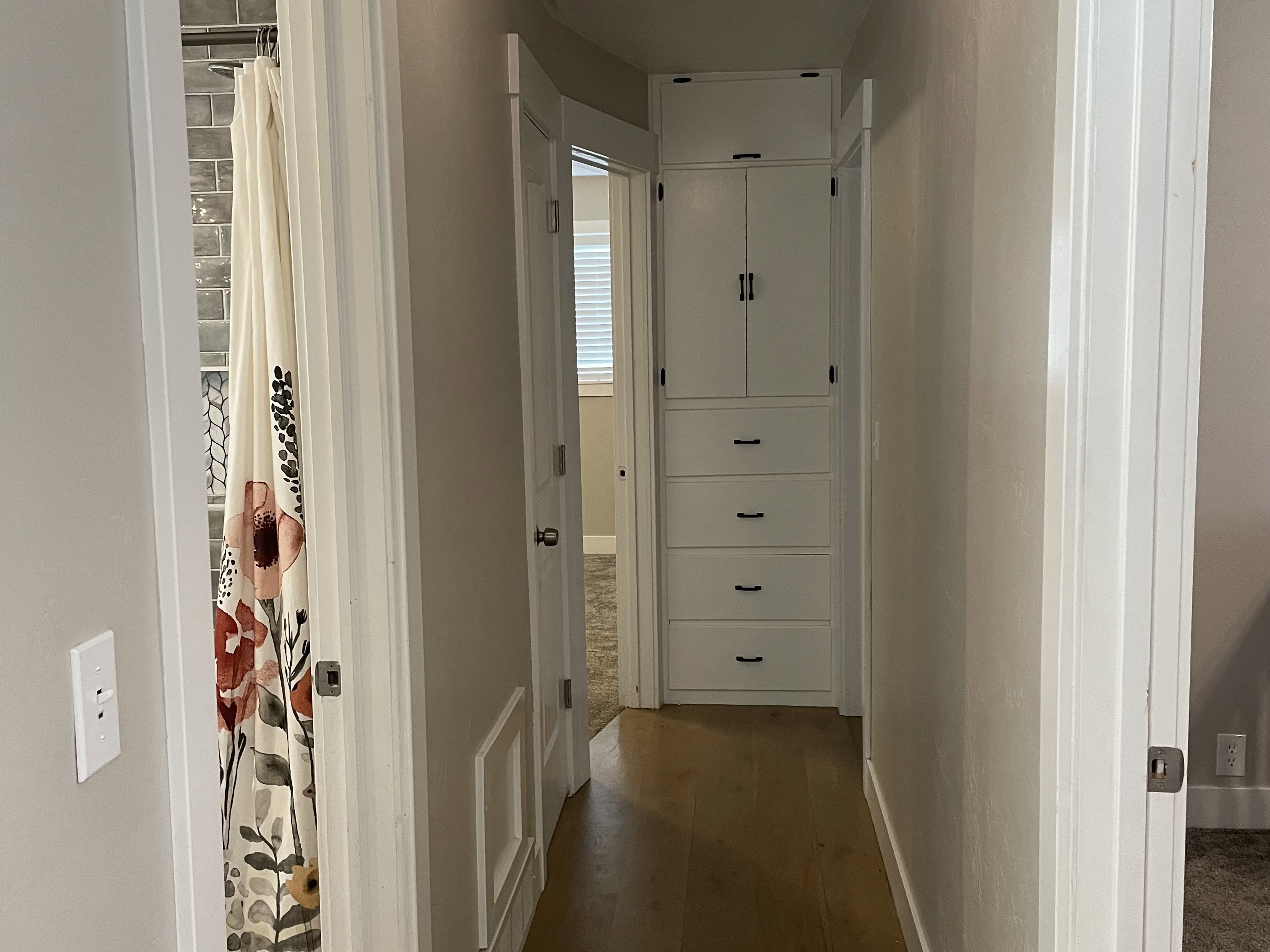 Hallway featuring built-in white cabinetry with black hardware, wood-finish flooring, and a bath area with subway tile surround