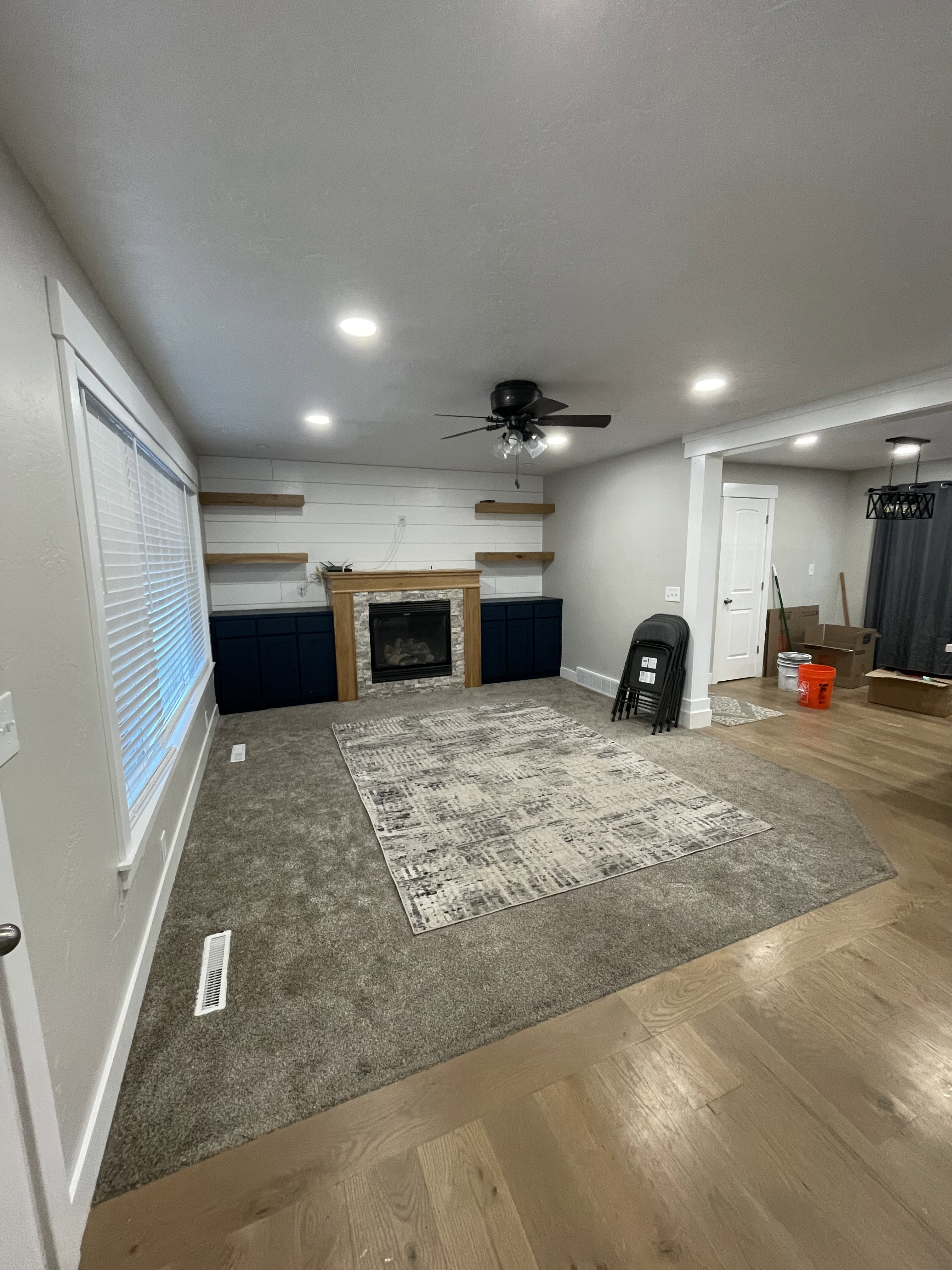 Living area featuring a fireplace with stone surround and wood mantle, built-in cabinetry, floating wood shelves, recessed lighting, and a ceiling fan