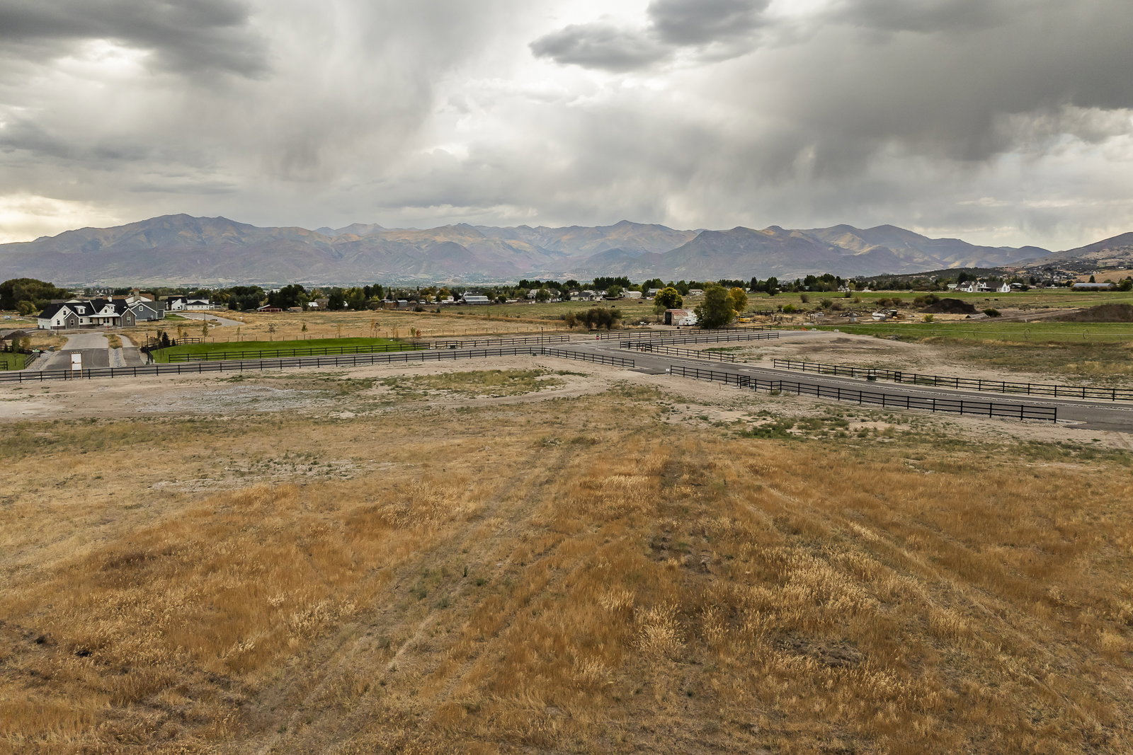 Expansive, undeveloped land featuring a partial paved road, a three-rail fence, and distant mountain scenery