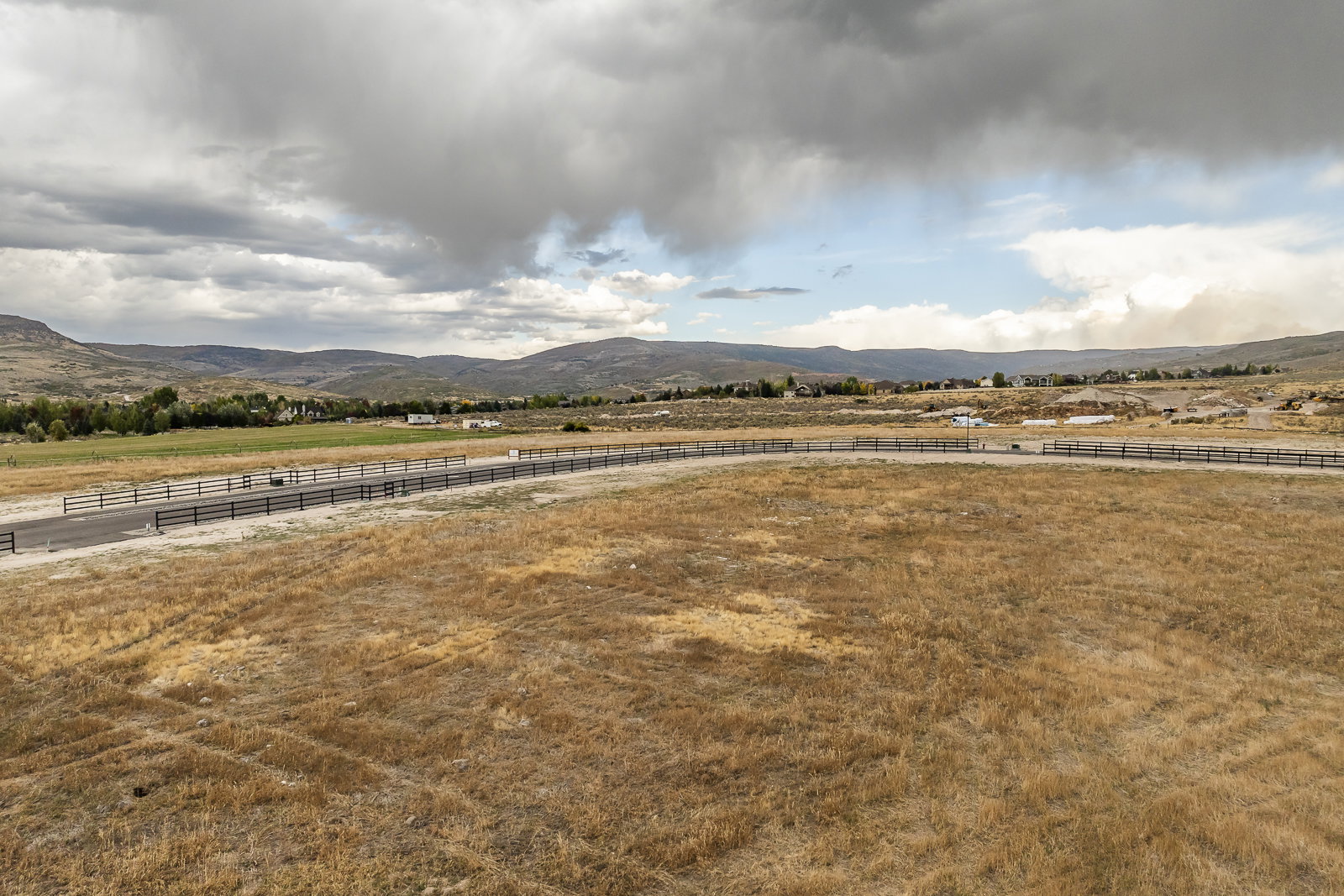 Expansive land parcel featuring a paved road, mountain backdrop, and distant residential structures