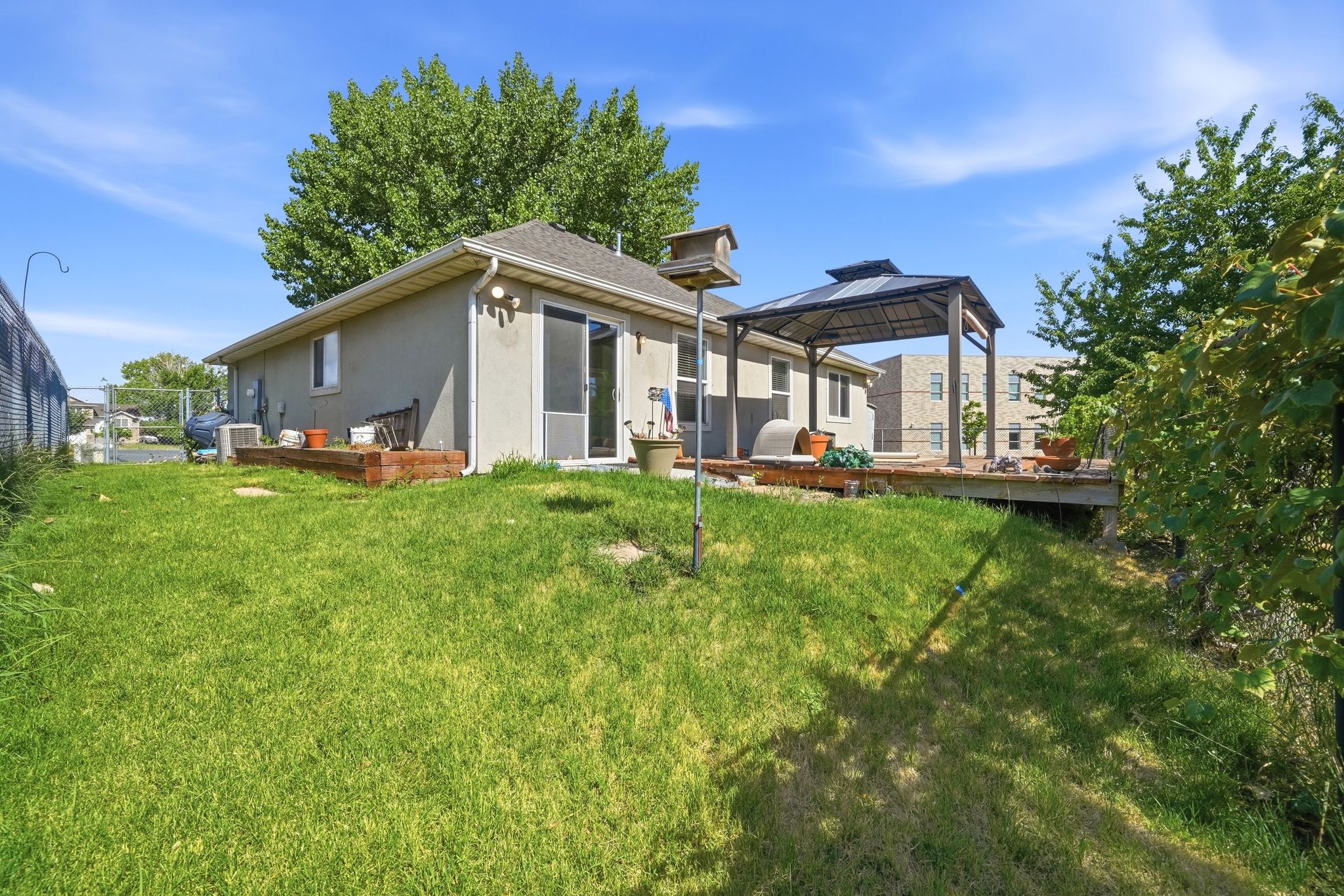 Rear exterior featuring a spacious wood deck, dedicated gazebo structure, sliding glass door access, and a sloped grass yard