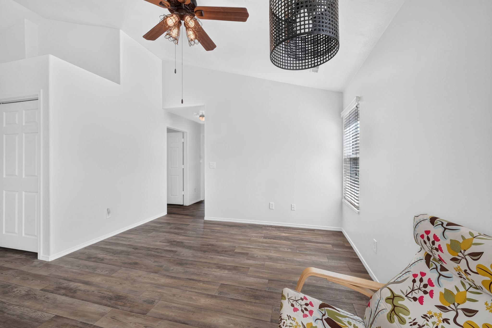 Spacious room featuring vaulted ceilings, wood-finish flooring, a ceiling fan, and a contemporary light fixture