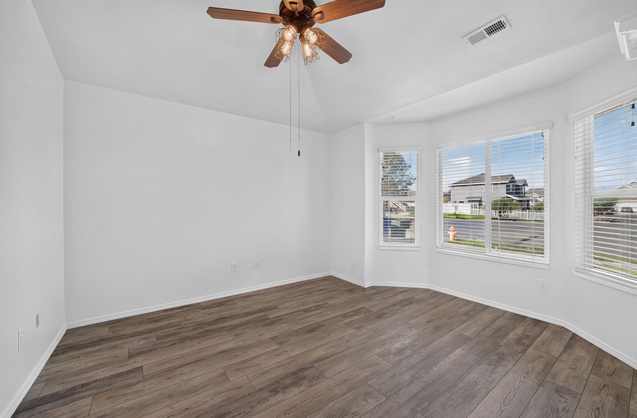 Bay window design with multiple windows, wood-finish flooring, white wall tones, and a ceiling fan with integrated lighting