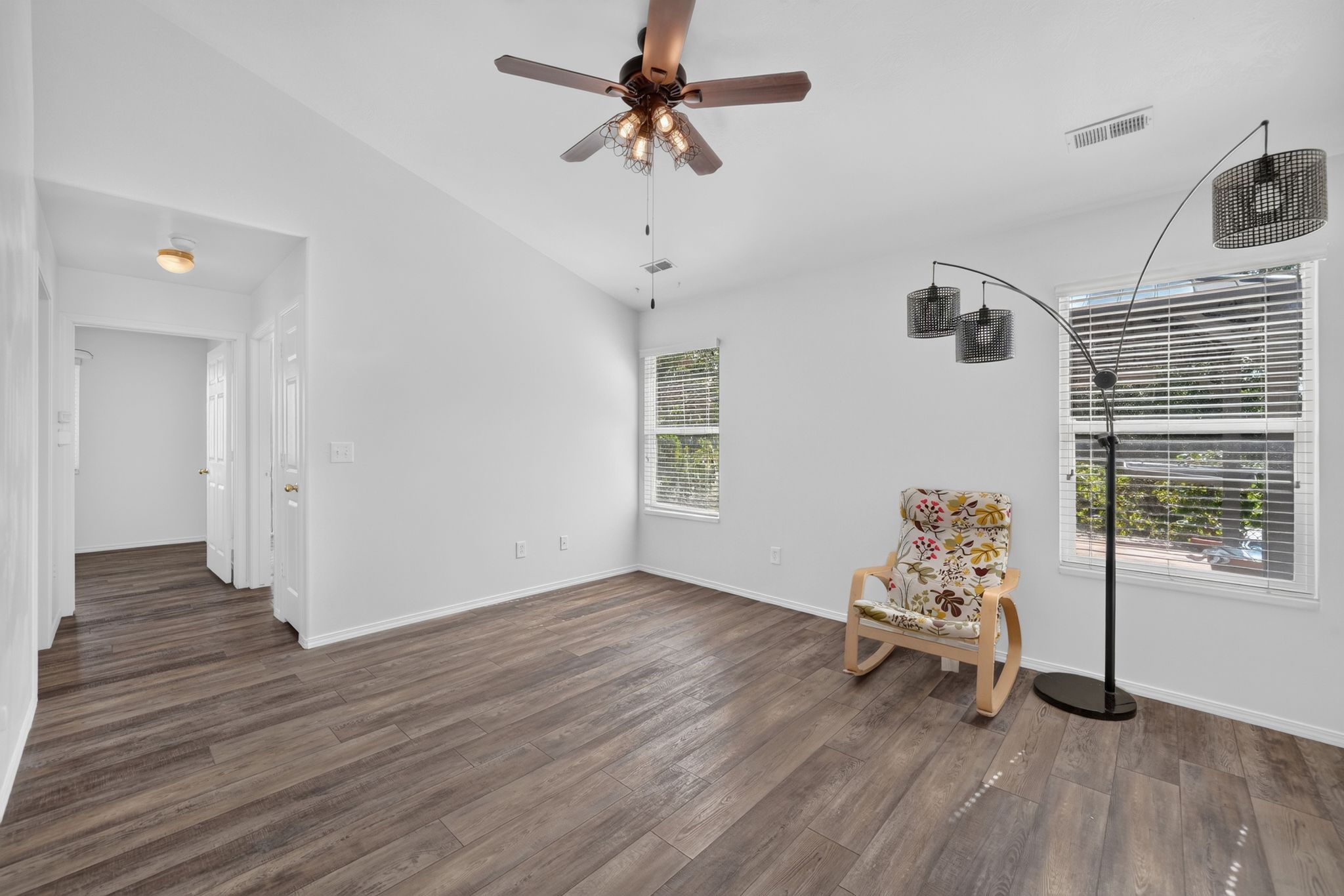 Spacious room featuring wood-finish flooring, white walls, and a ceiling fan with integrated lighting