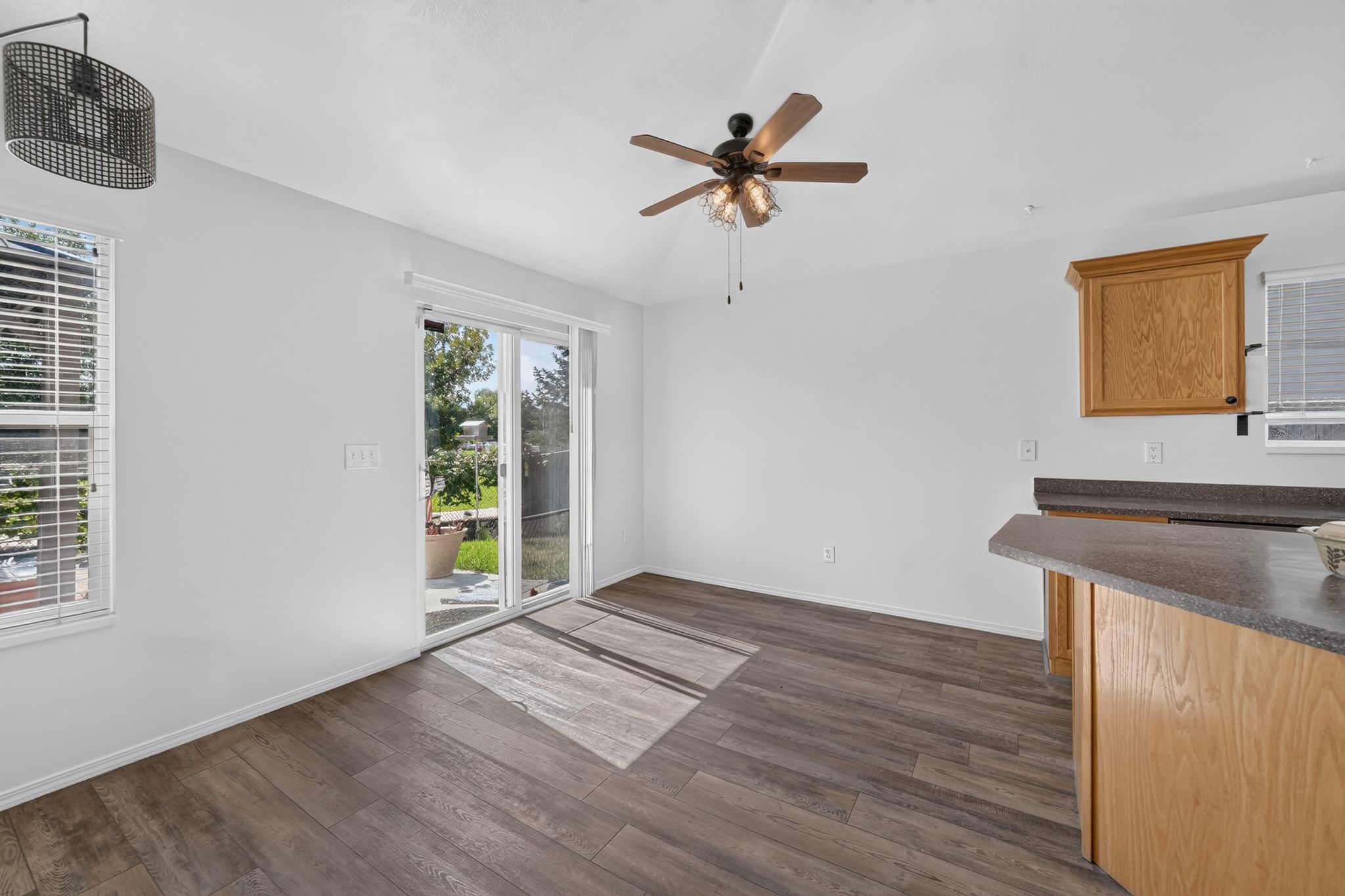 Spacious room featuring wood-finish flooring, a contemporary drum pendant light, and a ceiling fan with integrated lighting