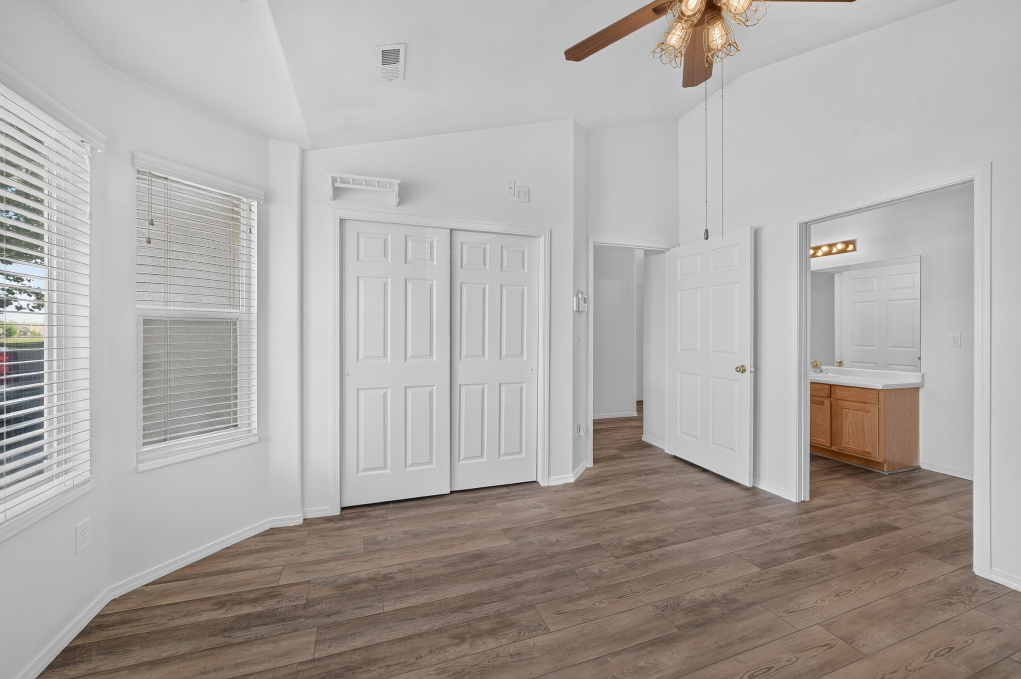 Vaulted ceiling room featuring wood-finish flooring and dual windows with blinds