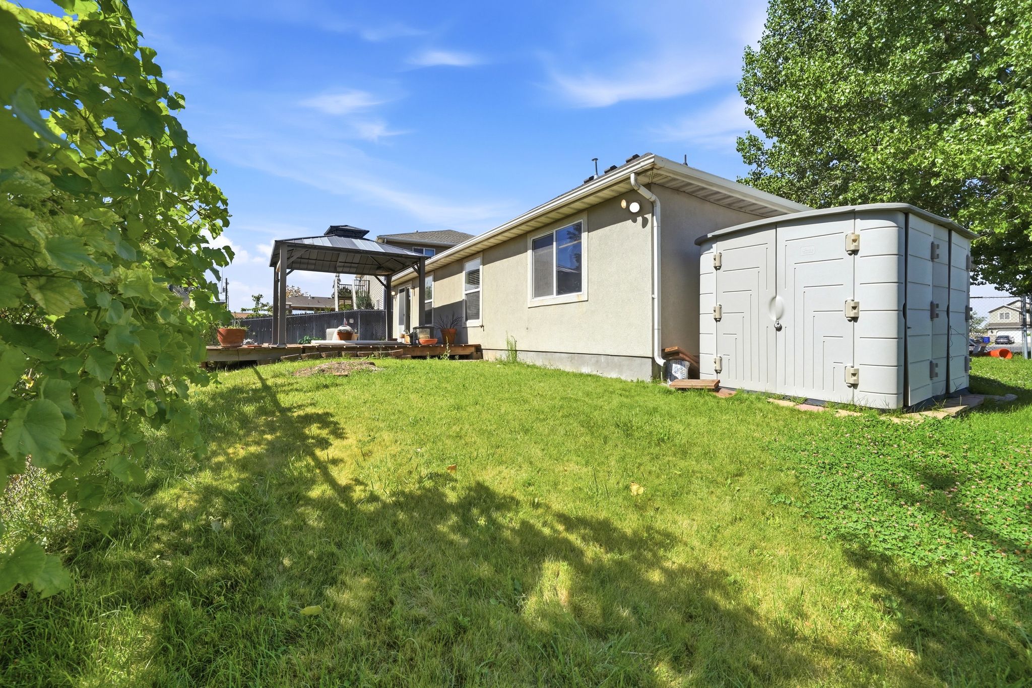 Expansive backyard featuring a gazebo-covered deck, a storage shed, and a stucco-sided exterior