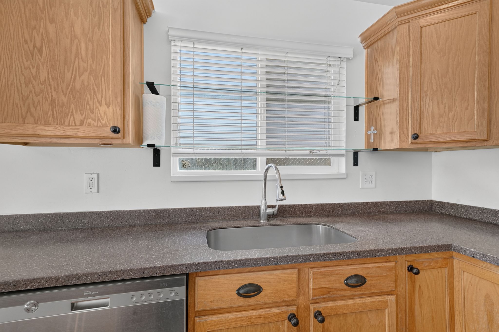 Kitchen featuring wood cabinetry, speckled countertops, a stainless steel sink with a gooseneck faucet, a window with blinds, and a built-in dishwasher