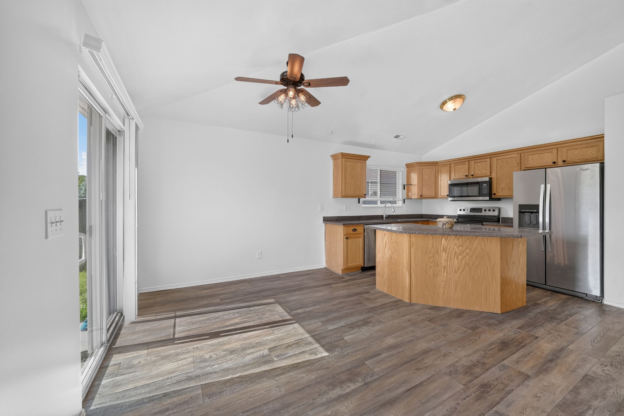 Open-concept kitchen and dining area featuring wood-finish flooring, vaulted ceilings, and a ceiling fan