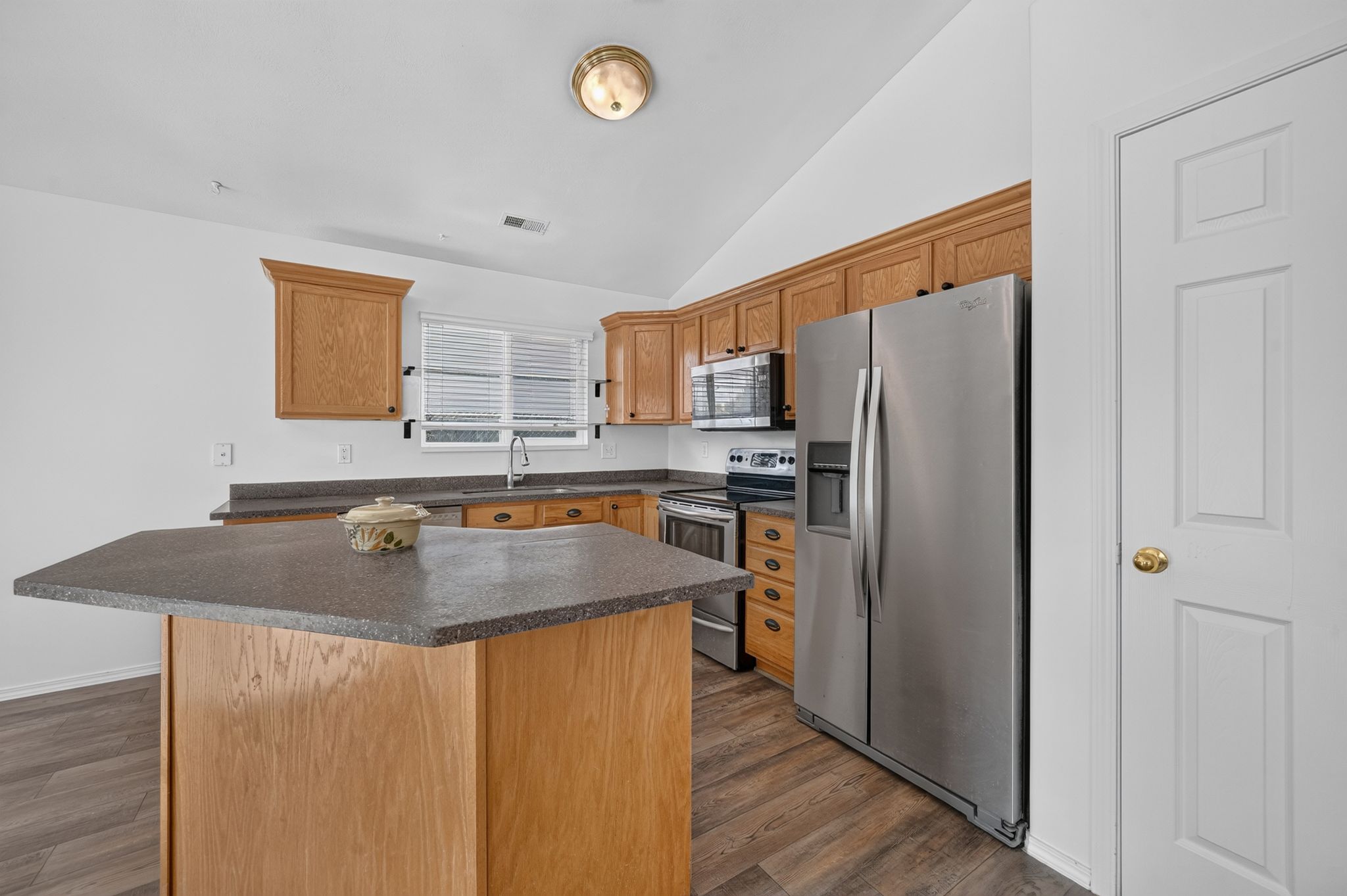Kitchen featuring wood cabinetry, stainless steel appliances, a corner sink, a central island with a solid surface countertop, and wood-finish flooring