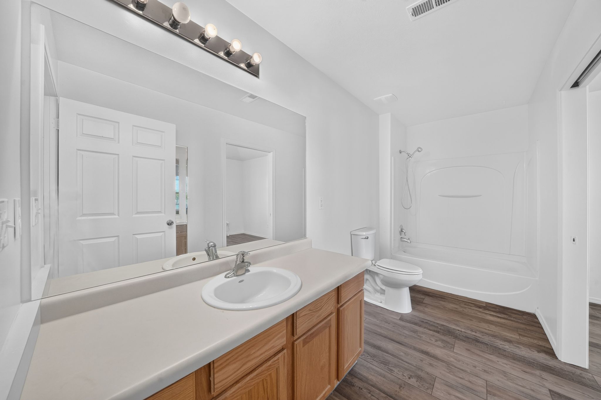 Bathroom with wood-finish flooring, a single vanity with a white basin sink, a large wall-mounted mirror, and a combined shower and tub unit