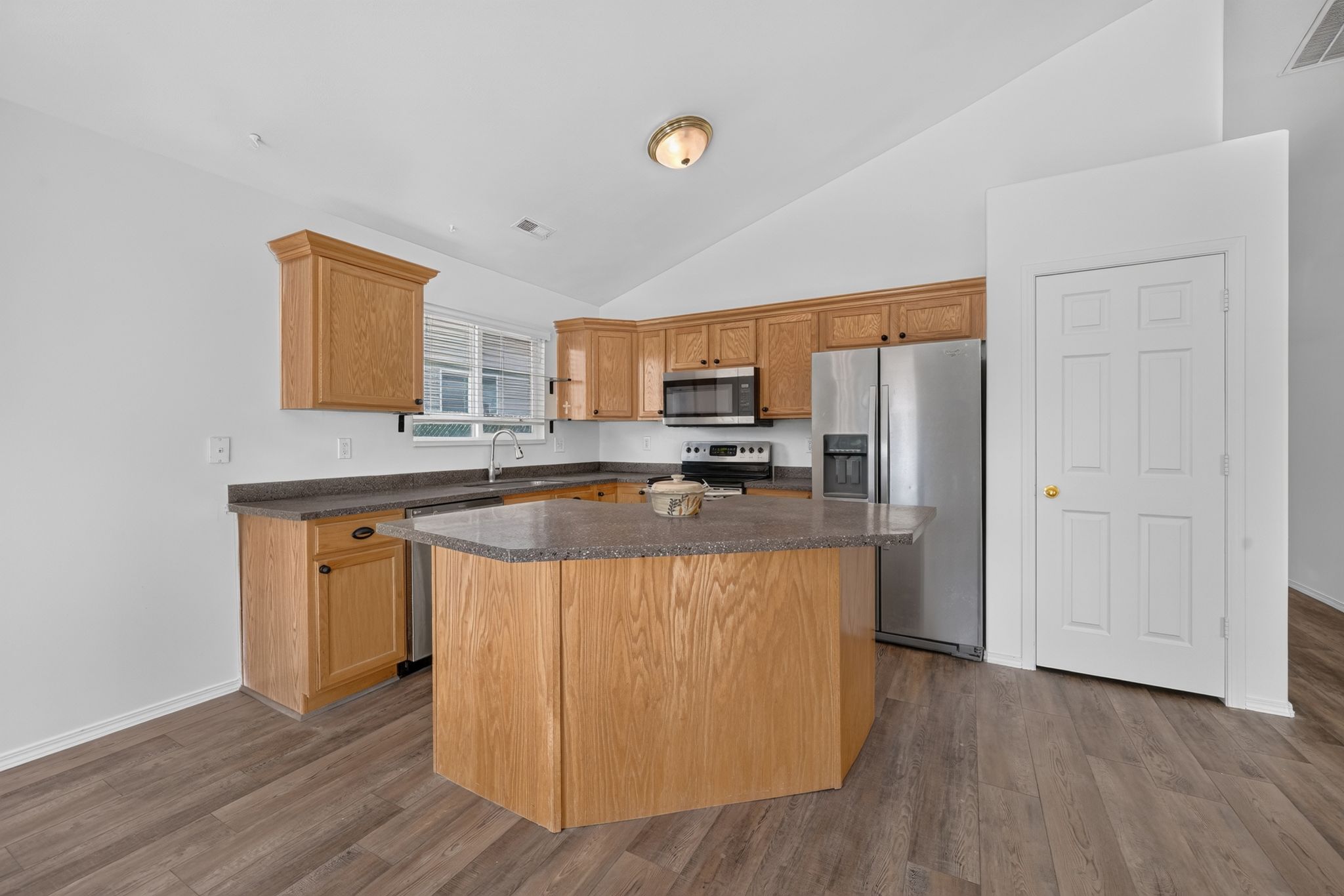 Kitchen featuring wood-finish flooring, a central island with a stone-finish countertop, stainless steel appliances, and natural wood cabinetry