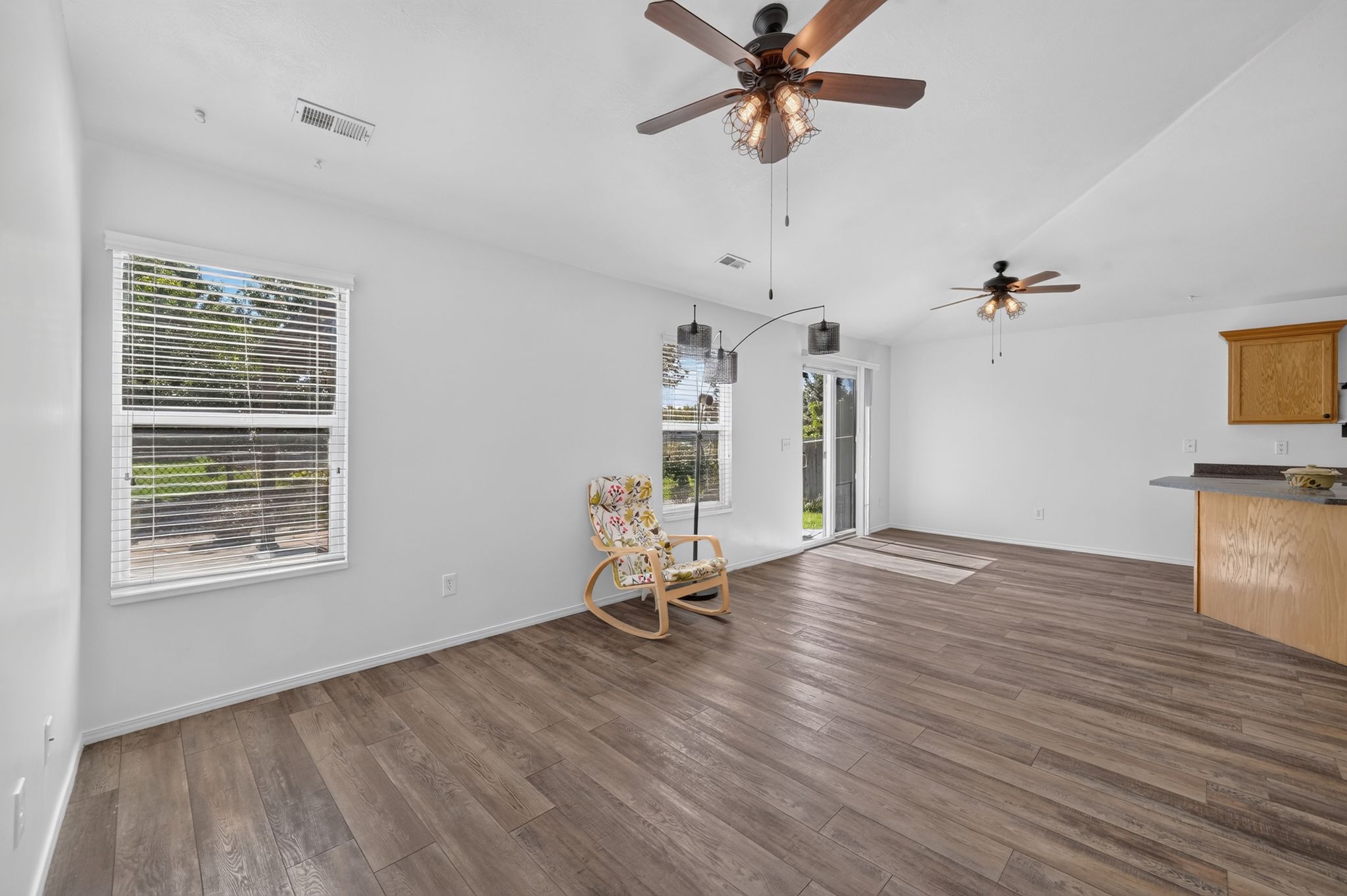 Spacious living area featuring wood-finish flooring, white walls, and multiple ceiling fans