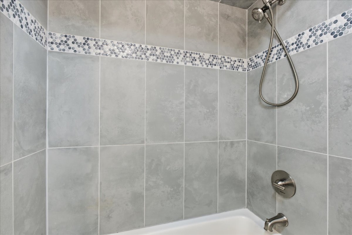 Bathtub shower combination featuring large format grey wall tiles, a decorative mosaic tile accent band, and brushed nickel fixtures