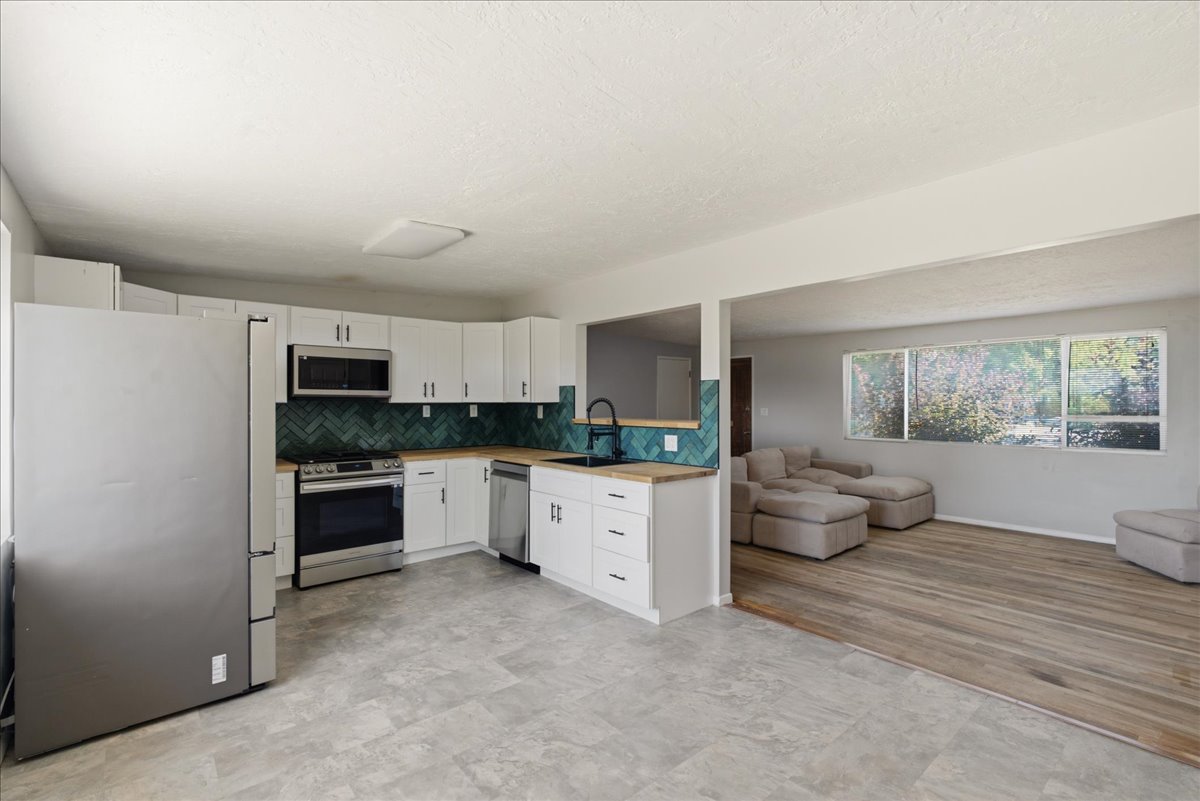 Modern kitchen featuring white cabinetry, stainless steel appliances, butcher block style countertops, and a teal herringbone tile backsplash