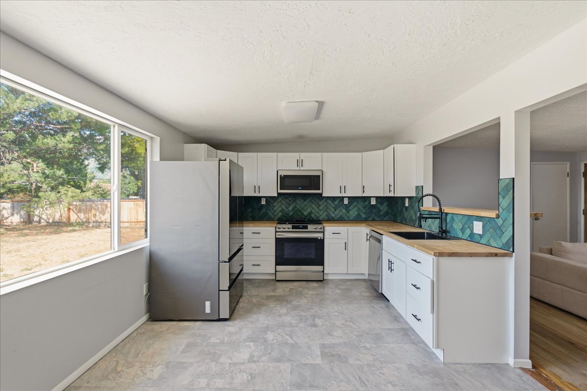 Contemporary kitchen featuring white cabinetry, wood-finish countertops, and a green herringbone tile backsplash