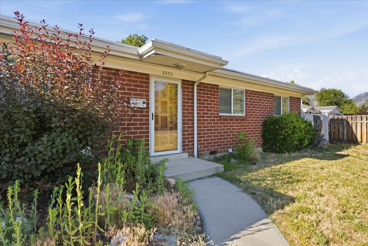 Brick exterior featuring a concrete walkway, established shrubbery, and a front entry door with a glass panel